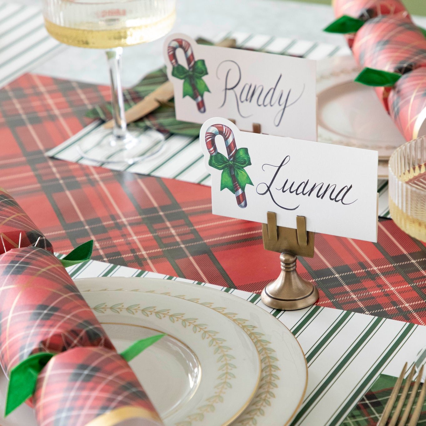 The Candy Cane Place Card with "Luanna" written on it, held up by the Brass Place Card Holder, on a festive table setting.