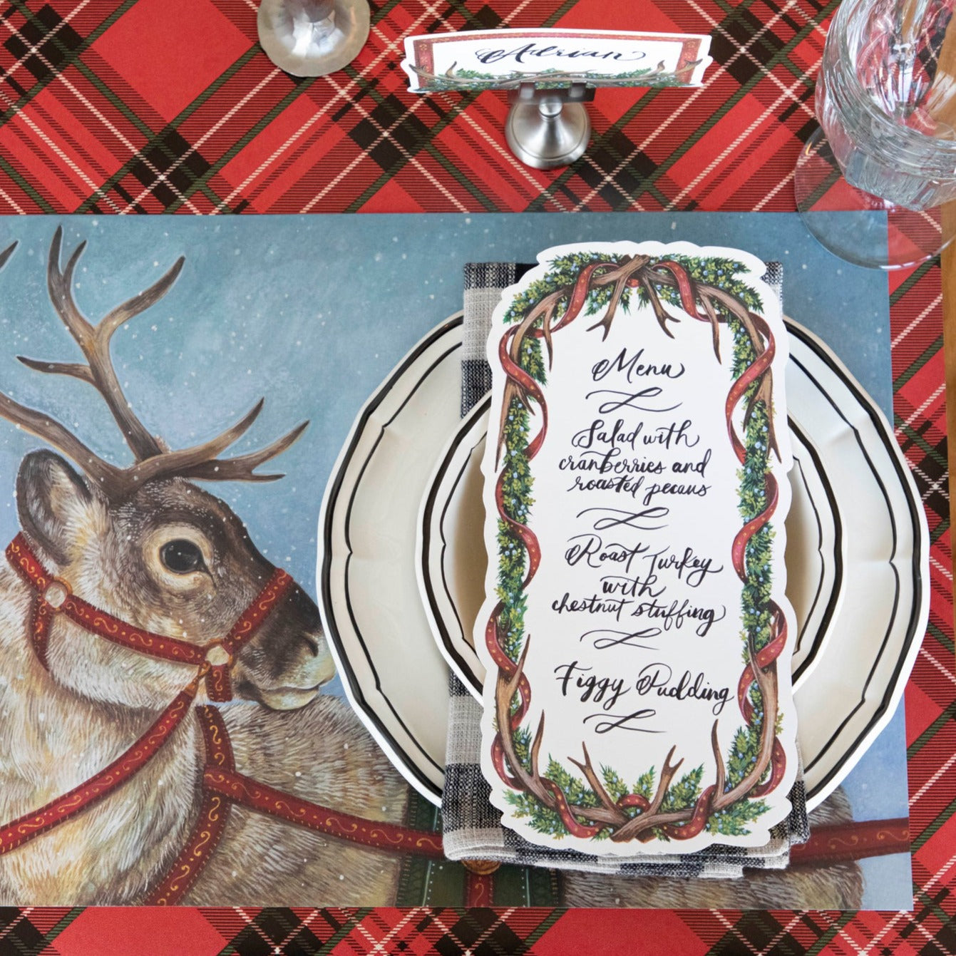 An Antler Garland Table Card with a menu written on it in lovely cursive, resting on the plate of a reindeer-themed Christmas place setting.