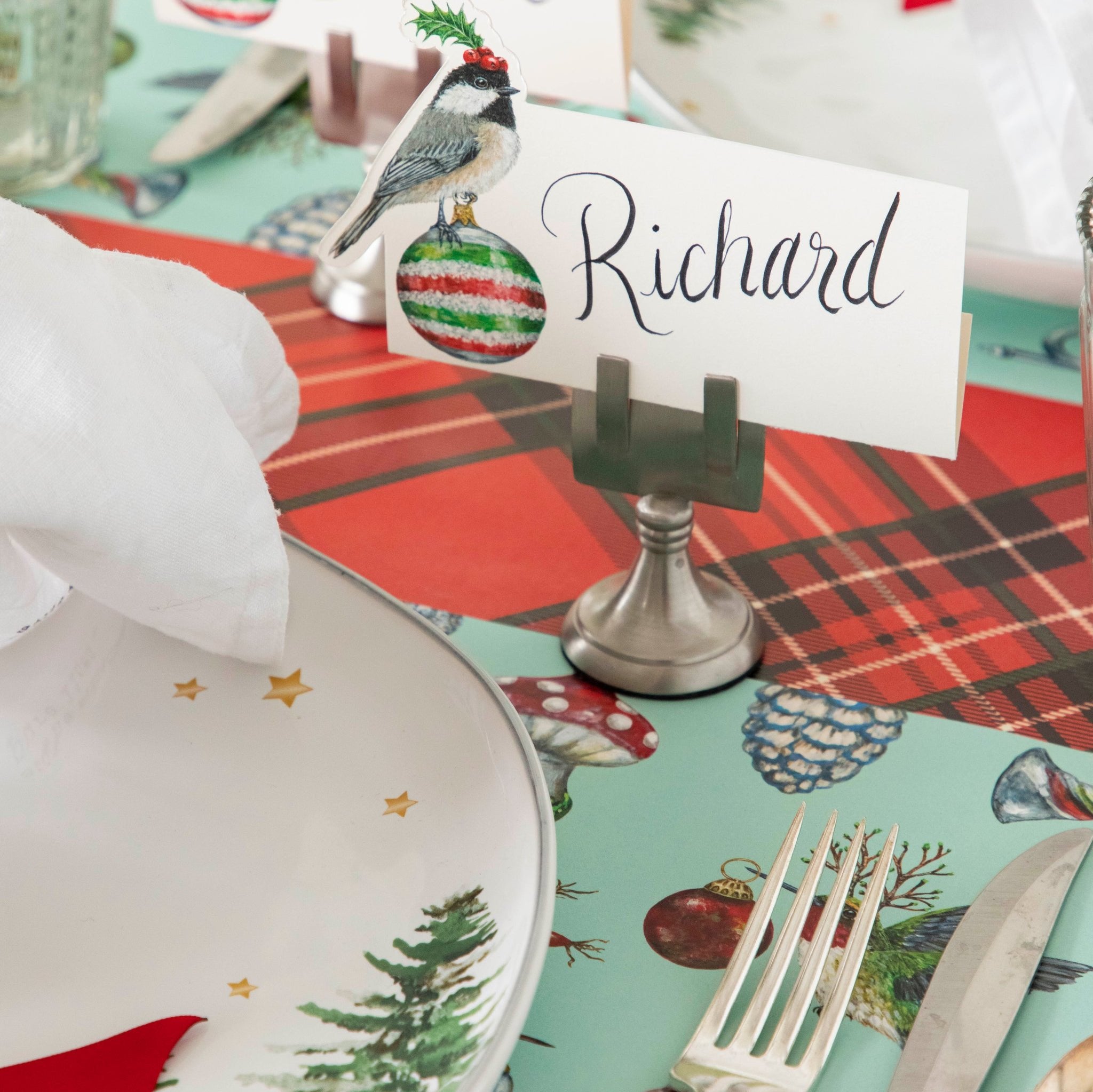 The Christmas Chickadee Place Card with the name "Richard" on it, being held up by the Silver Place Card Holder, on a festive place setting.