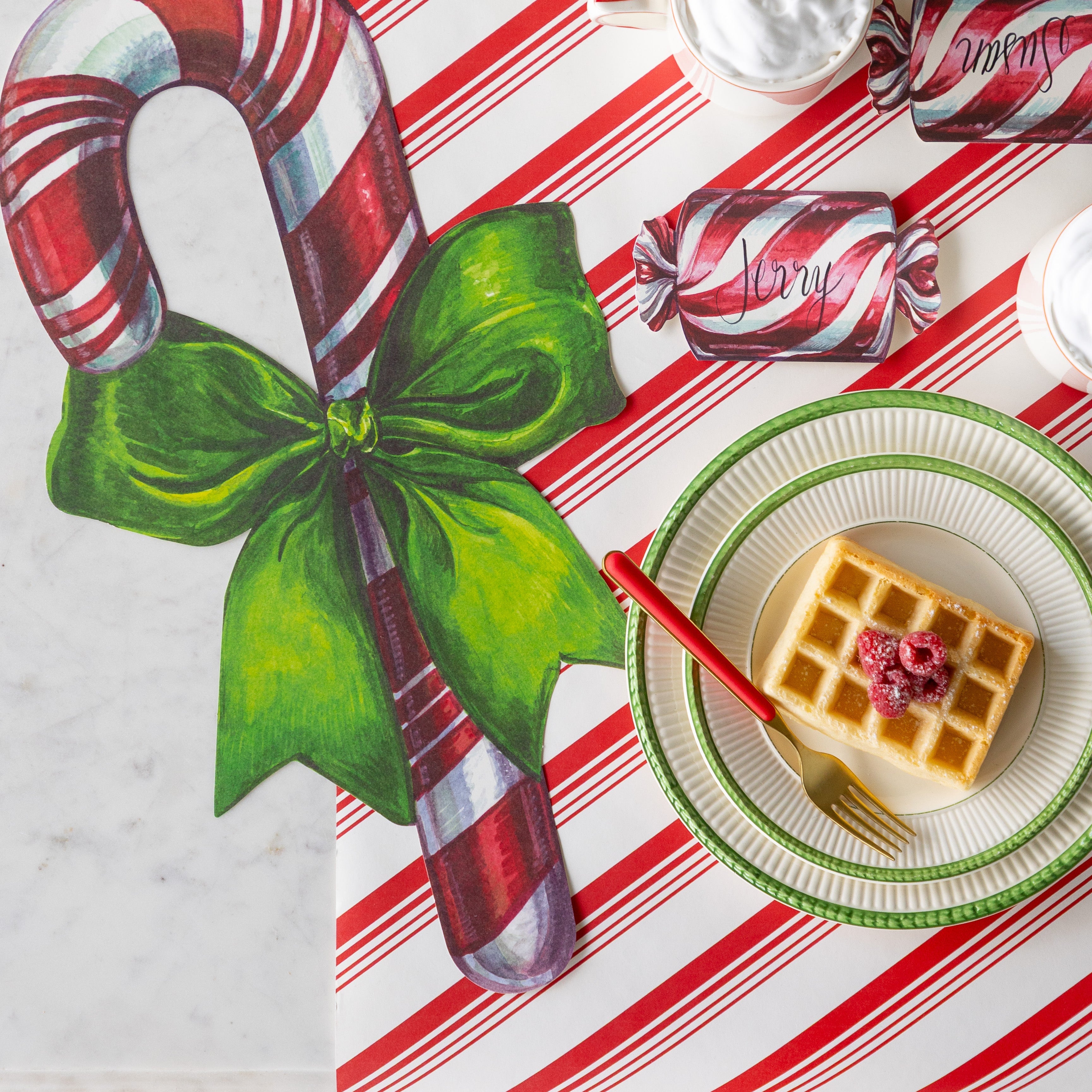 The Christmas Candy Place Card reading "Jerry" next to the Die-cut Candy Cane Placemat and behind two stacked plates with waffles and a fork on it.