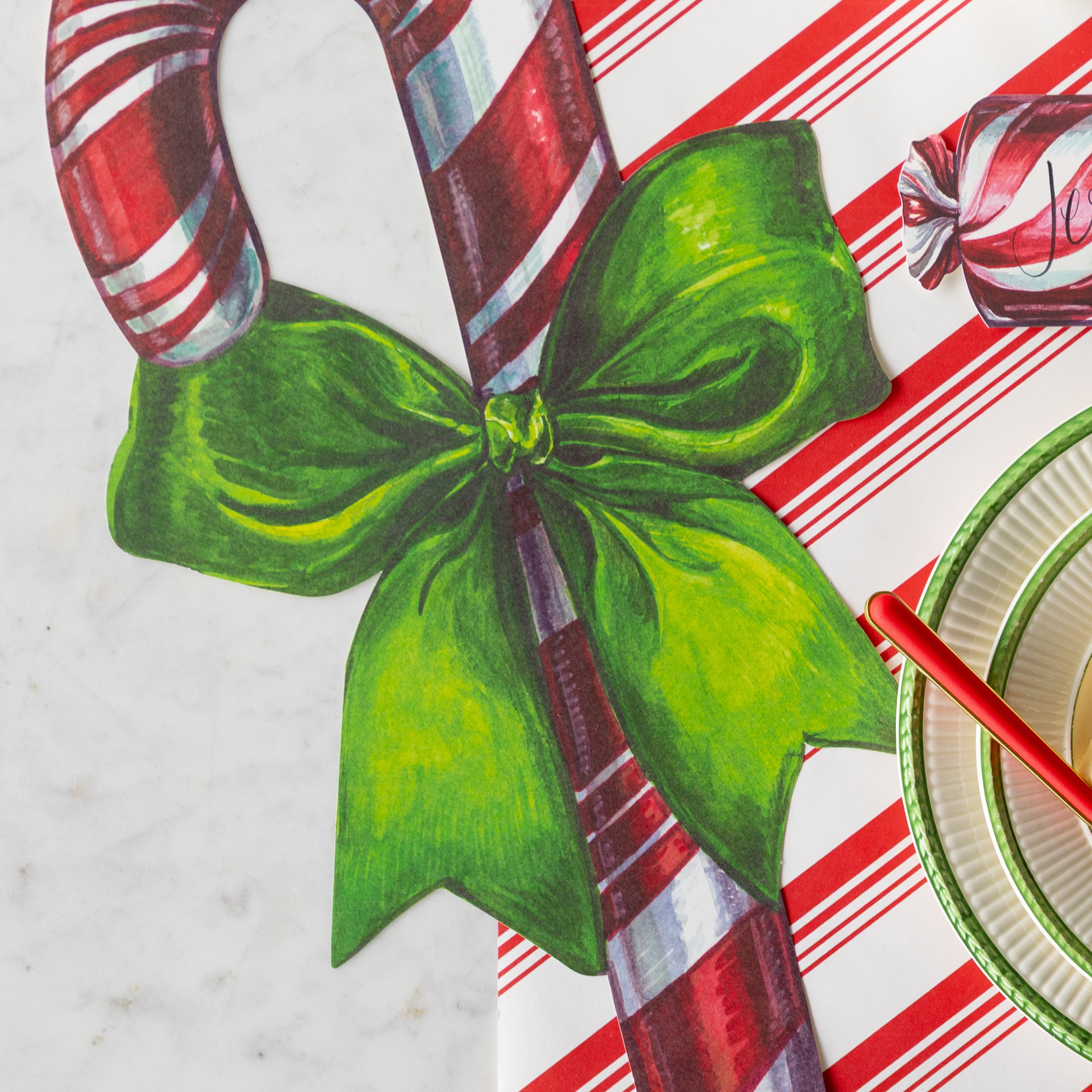 A close up of the Die-cut Candy Cane Placemat showing its green bow tied around the candy cane.