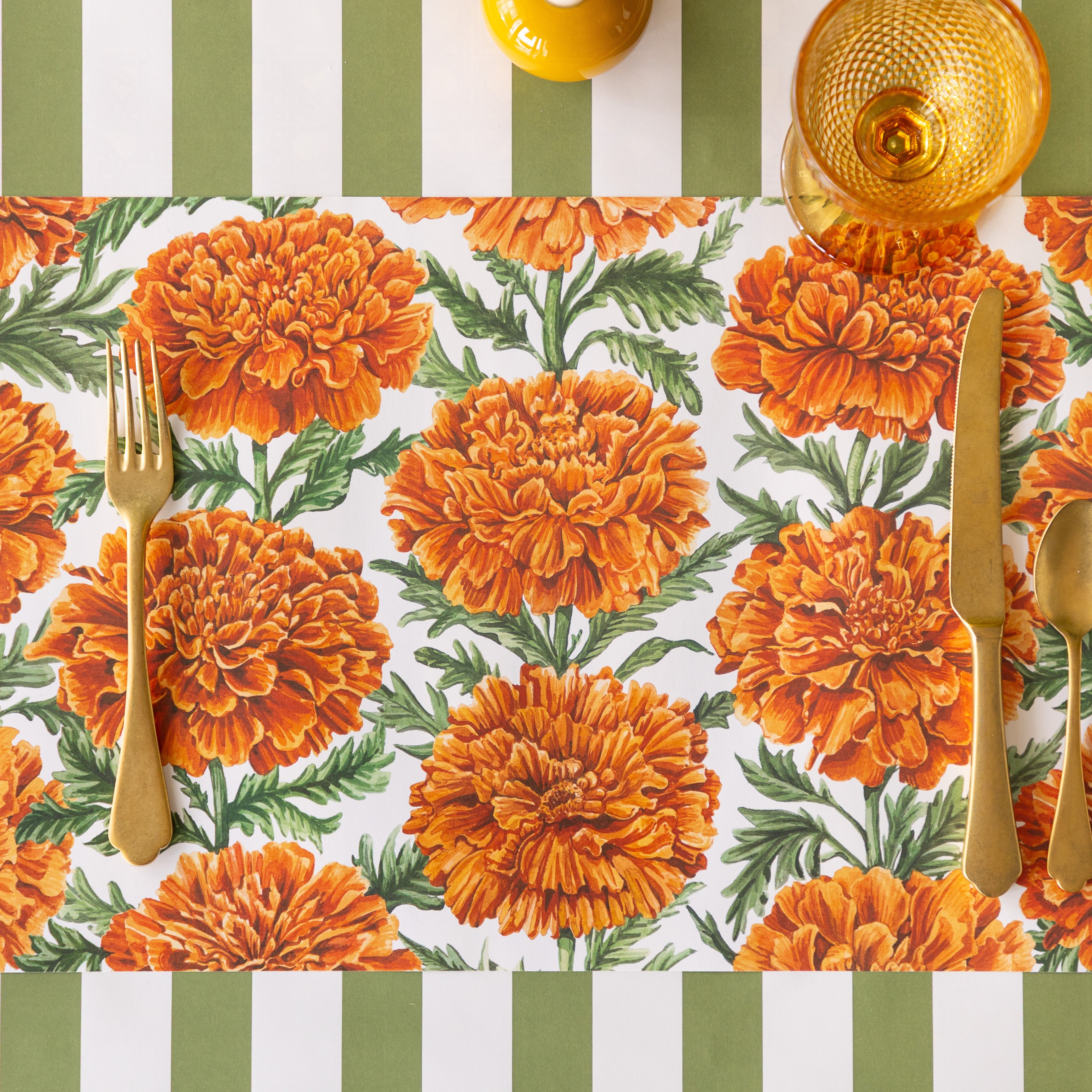 The Marigold Harvest Placemat with gold flatware and an orange glass atop, and Moss Classic Stripe Runner underneath.