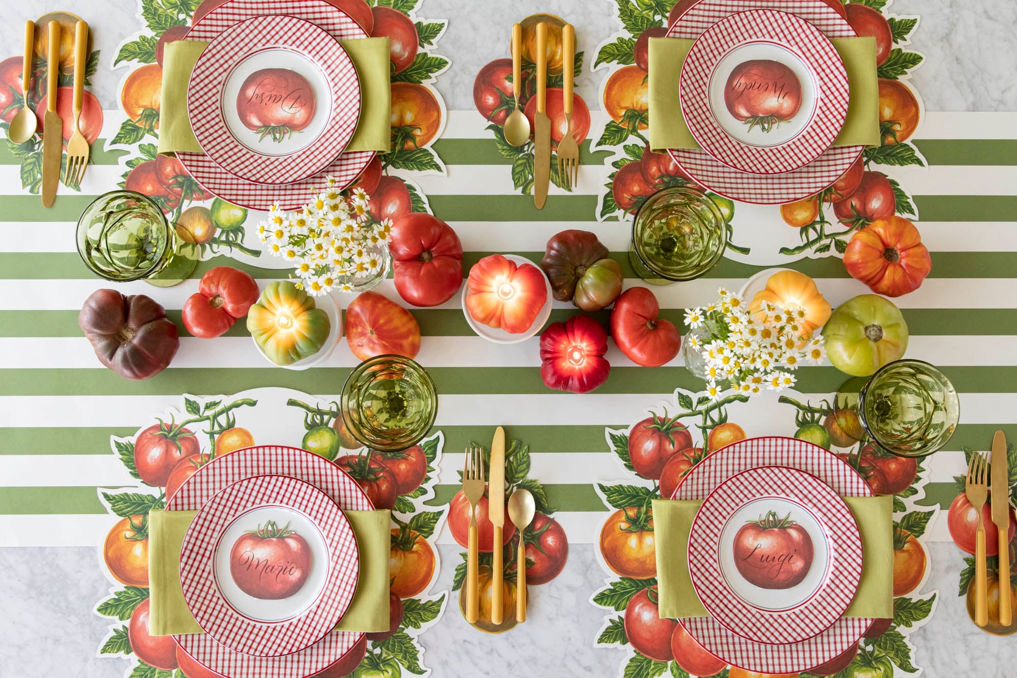Table set with Die-cut Tomato placemats on a green stripe runner with tomato shaped candles and real tomatoes artfully arranged down the table.