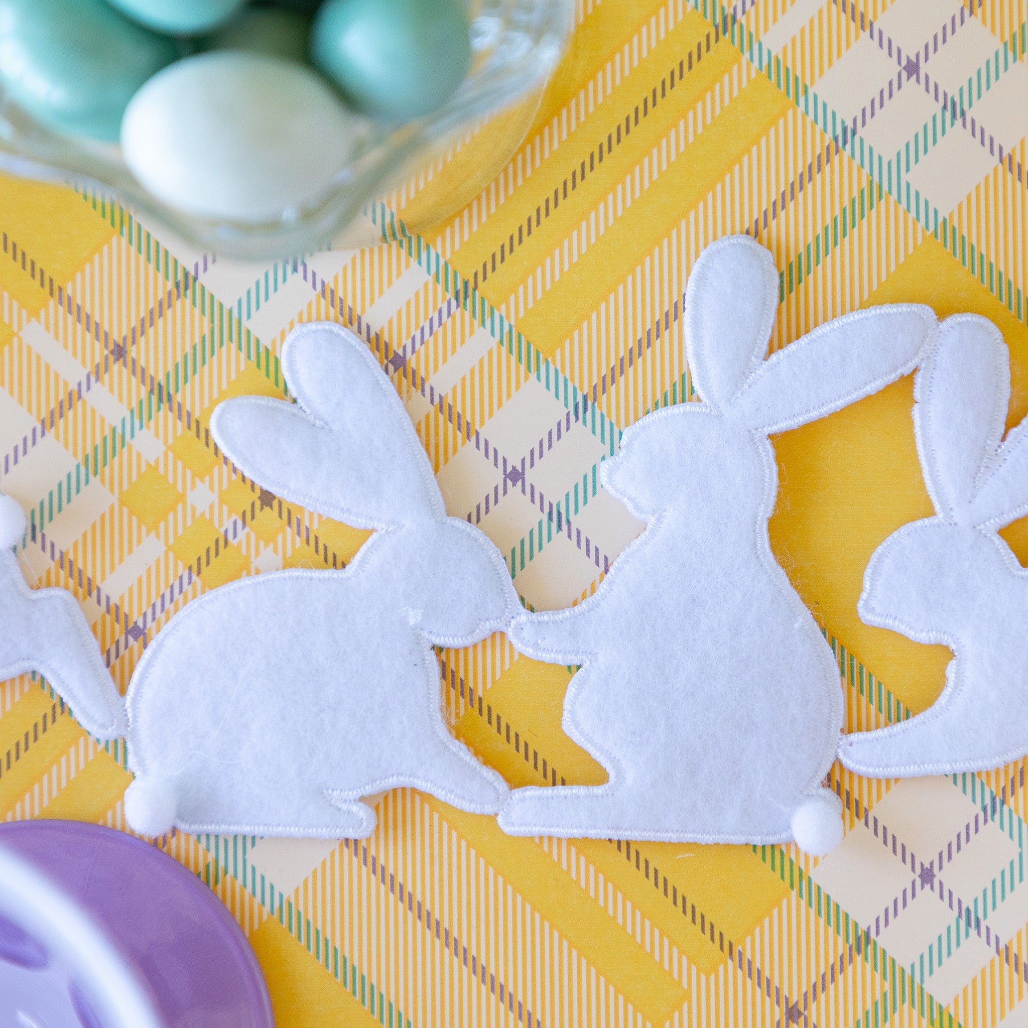 Rabbit Garland Ribbon with white appliqué rabbits made of felt running down a table with a yellow plaid runner and purple glasses on it.