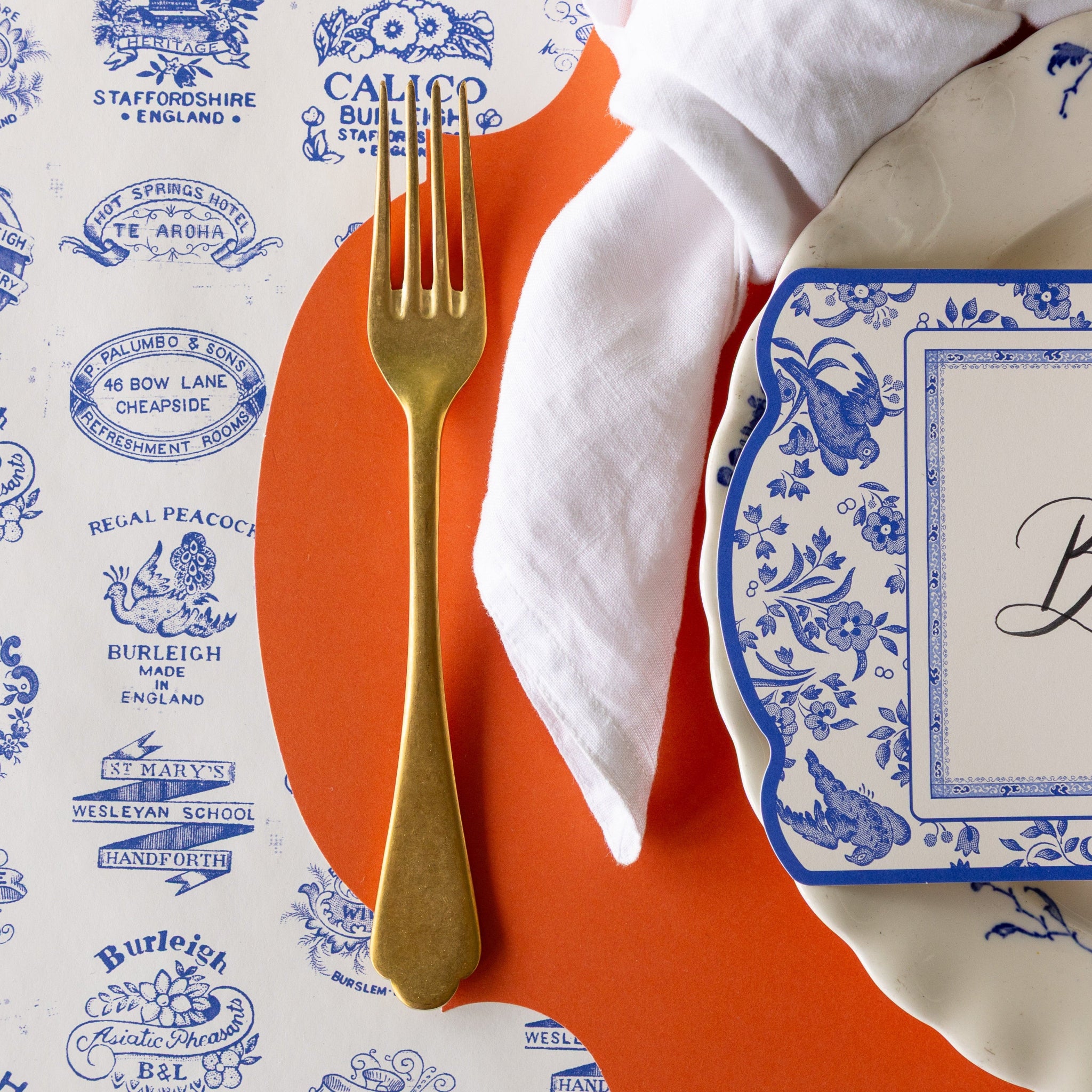 A place setting featuring the Orange French Frame Placemat with the Burleigh Heritage Runner underneath.