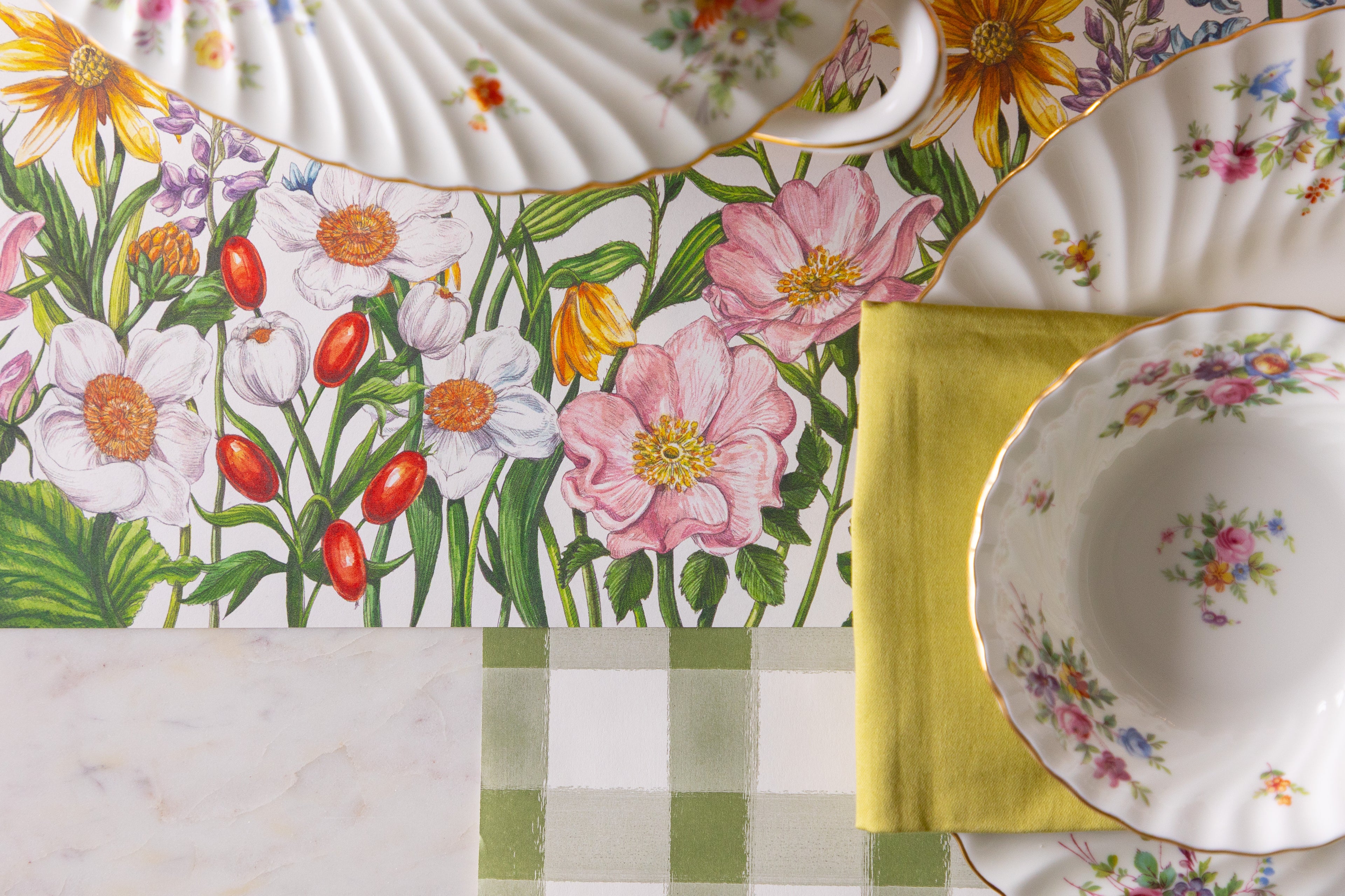 Floral-patterned plates on a marble surface with checkered and yellow napkins.
