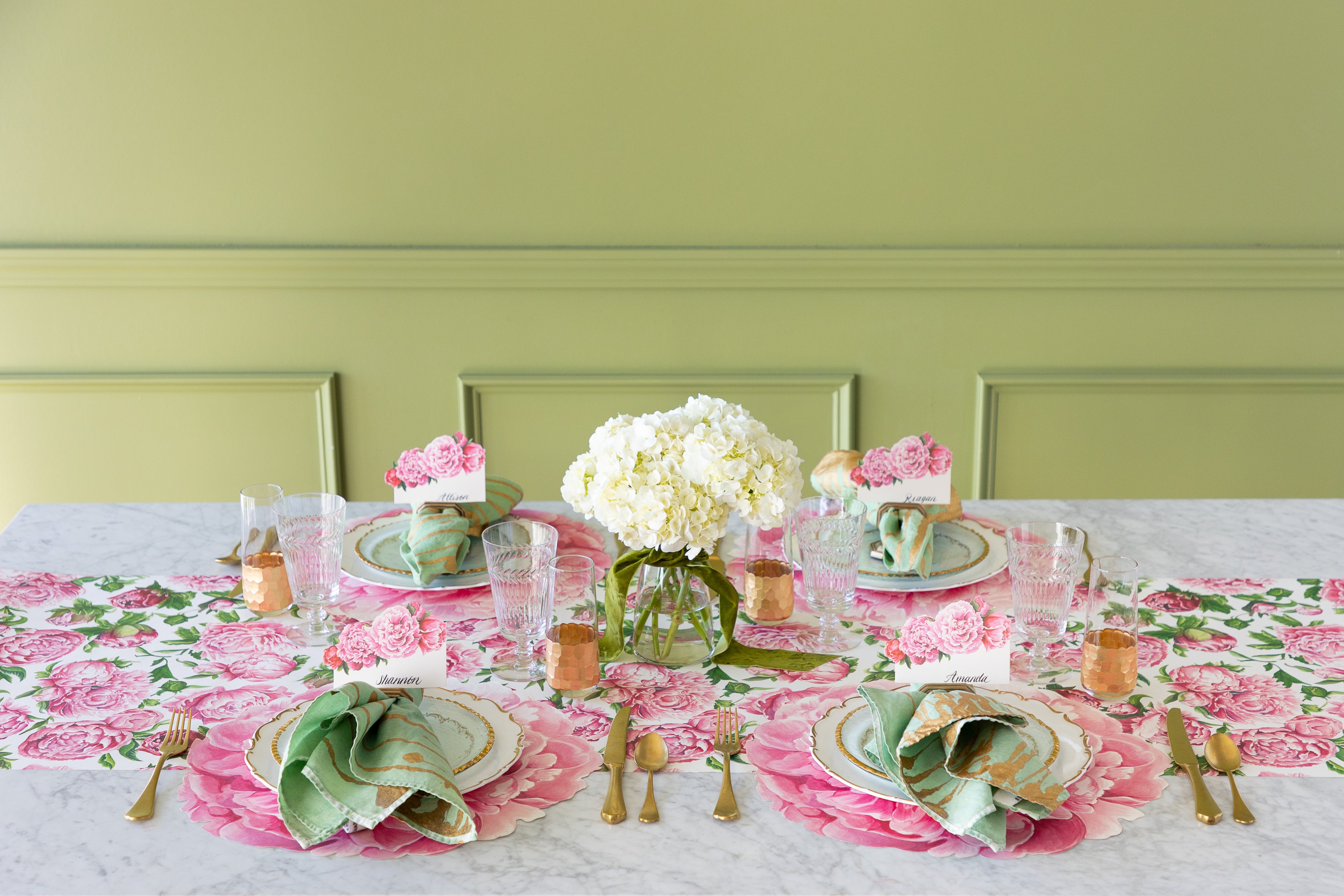 A decorative table setting with the Peonies in Bloom Runner, flowers, Die-cut Peony Placemats, decorative plates, Peonies Place Cards, marbled napkins and gold flatware.