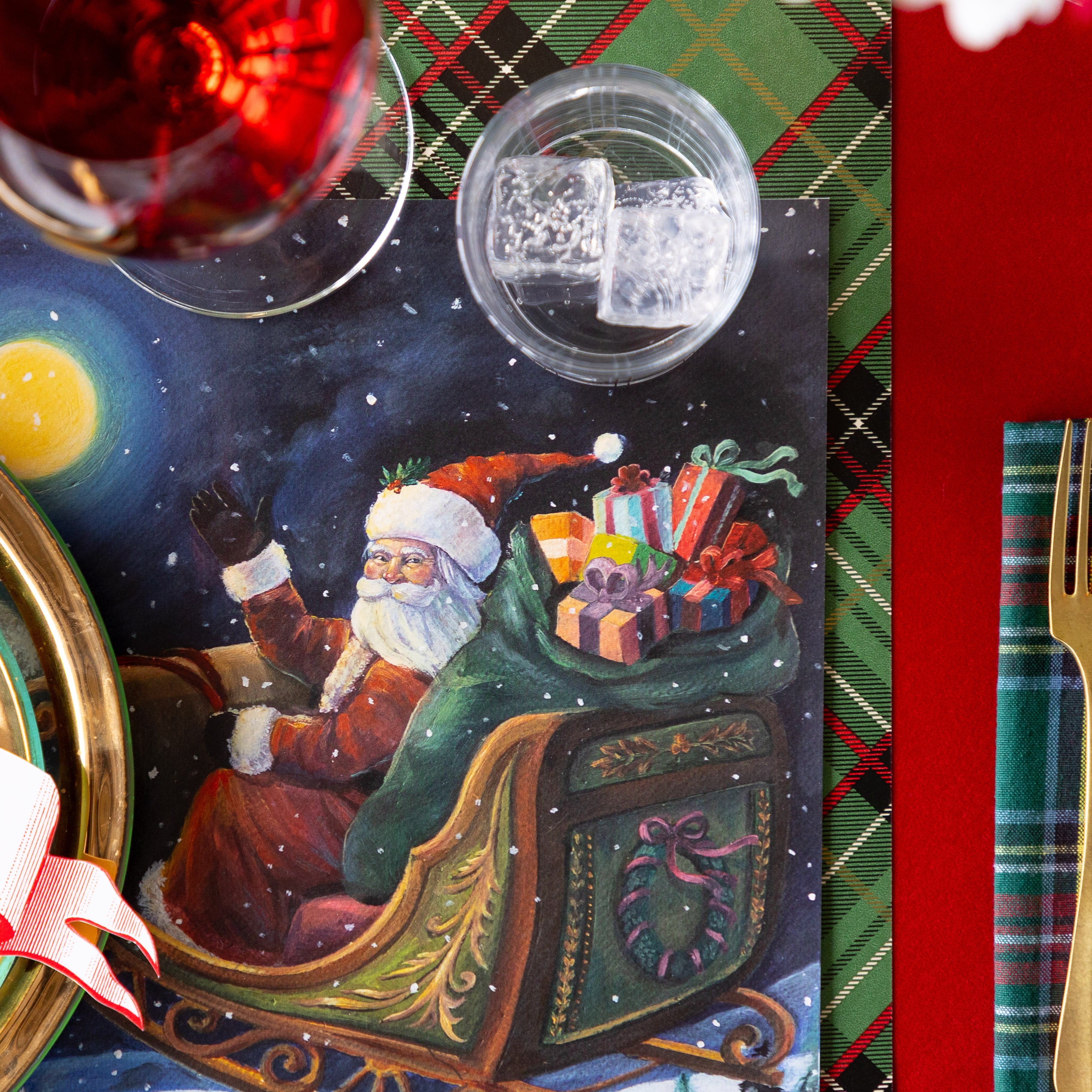 A close up of the Sleigh Ride Placemat under a place setting, showing Santa Claus in his sleigh with a sack of presents, waving.