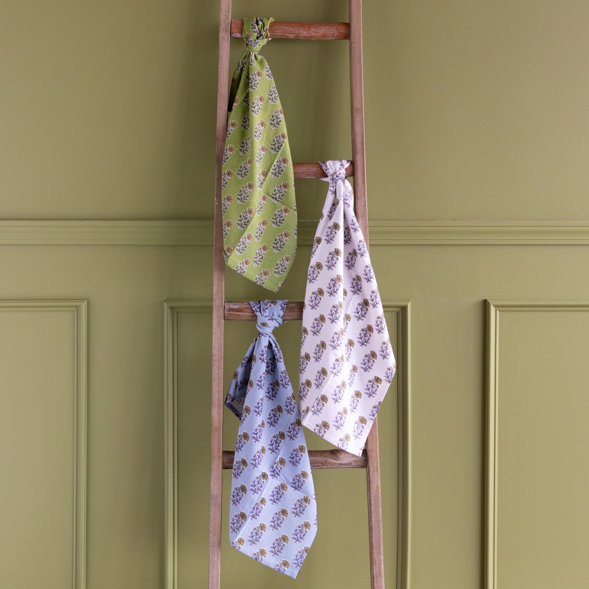 Wooden ladder with floral-patterned towels on a green paneled wall.