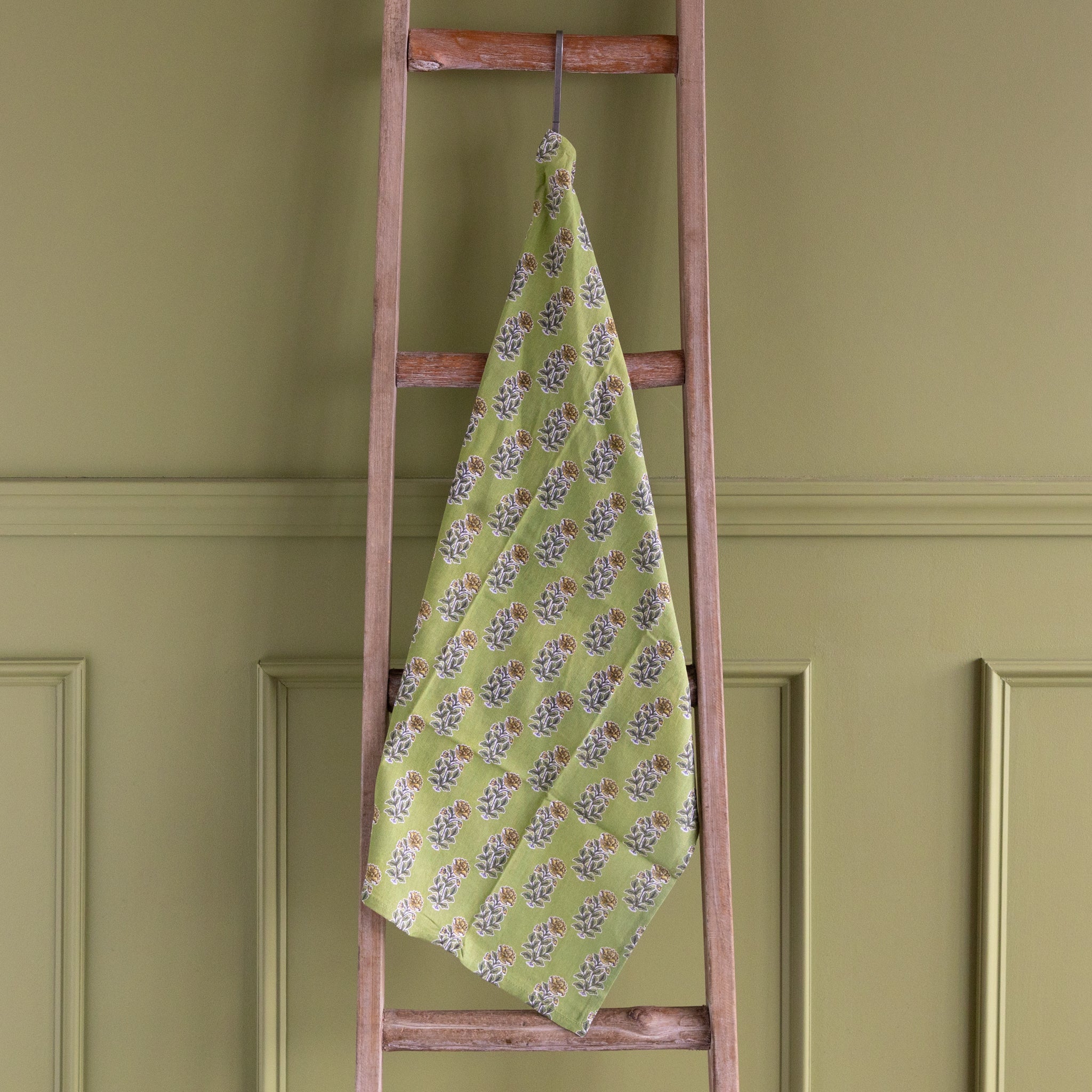 Green floral towel hanging on a wooden ladder against a green wall.