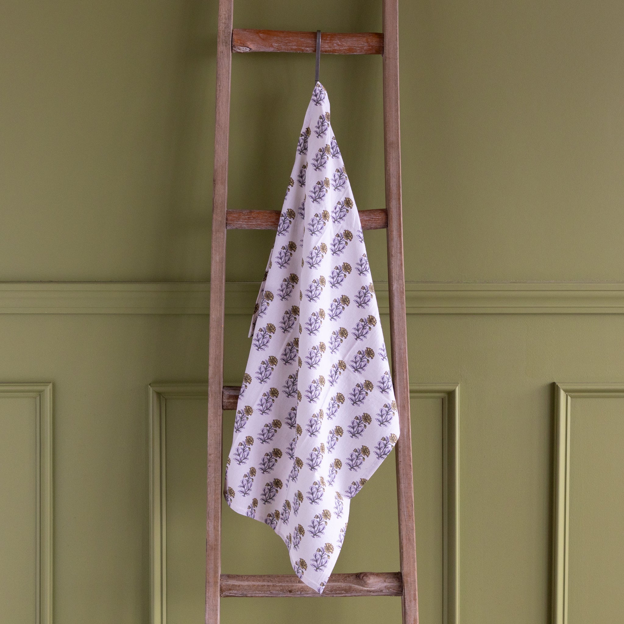Floral-patterned towel hanging on a wooden ladder against a green wall.
