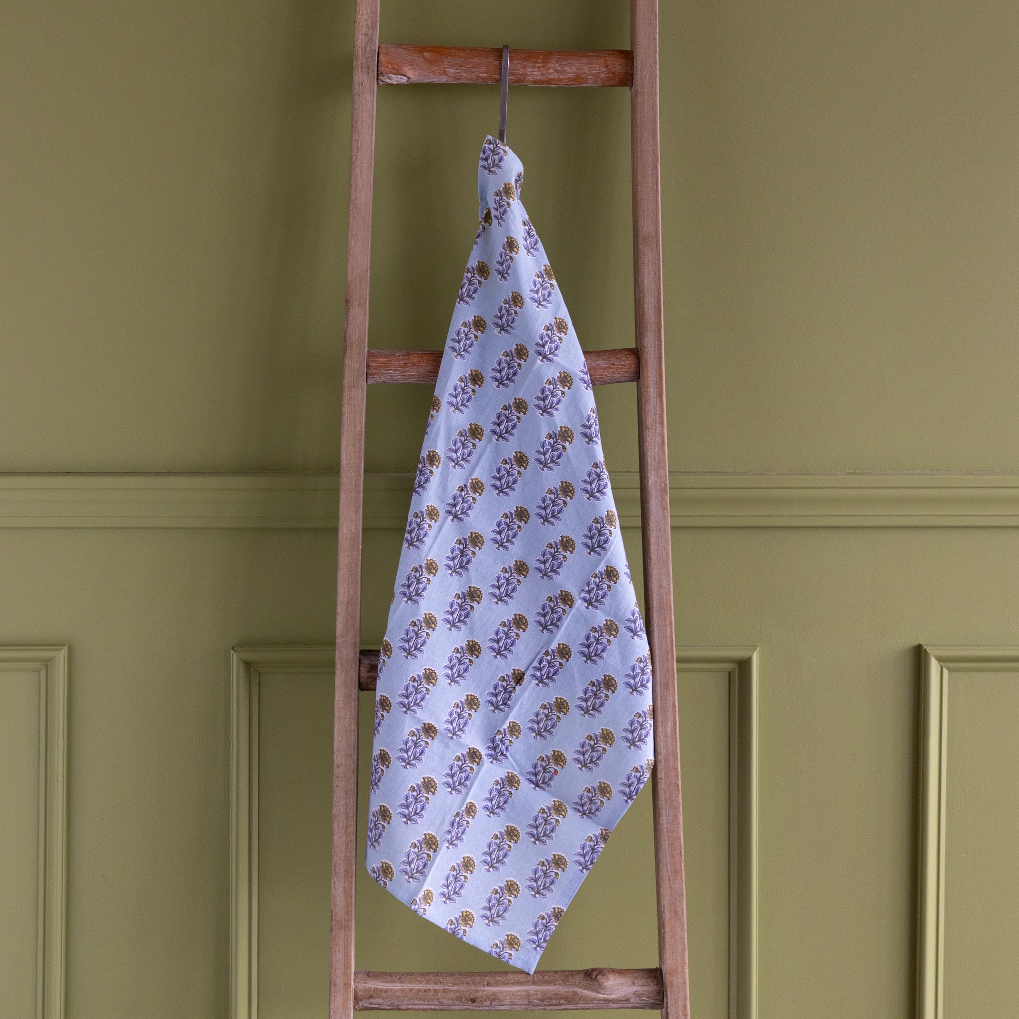 Floral-patterned towel hanging on a wooden ladder against a green wall.