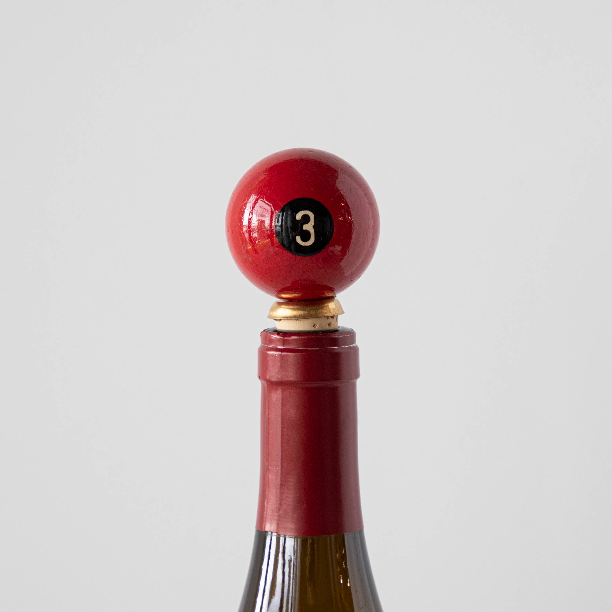 A red, number 3, Pool Ball Knobstopper in a wine bottle.