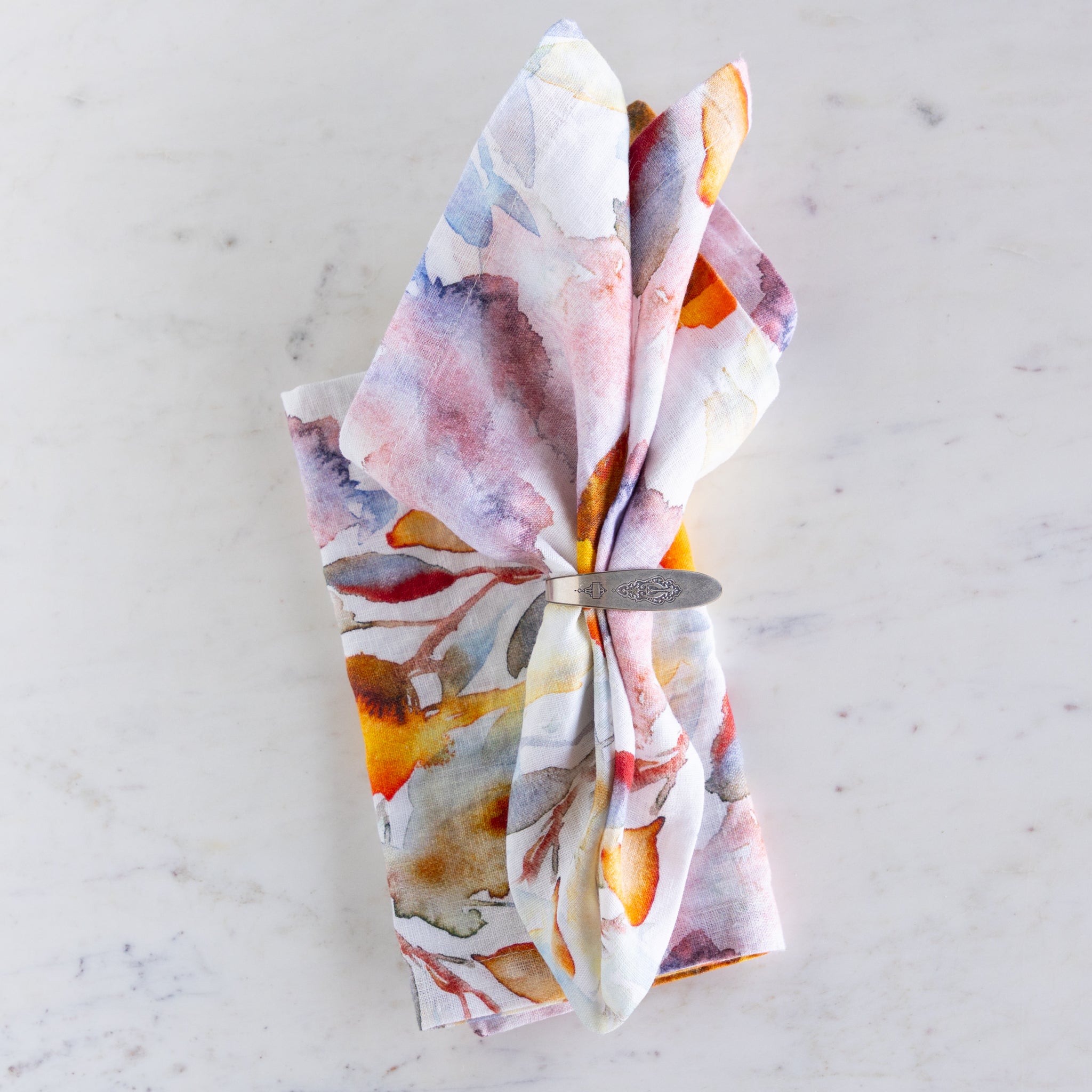 Colorful floral-patterned napkin with a metal napkin ring on a light marble background.