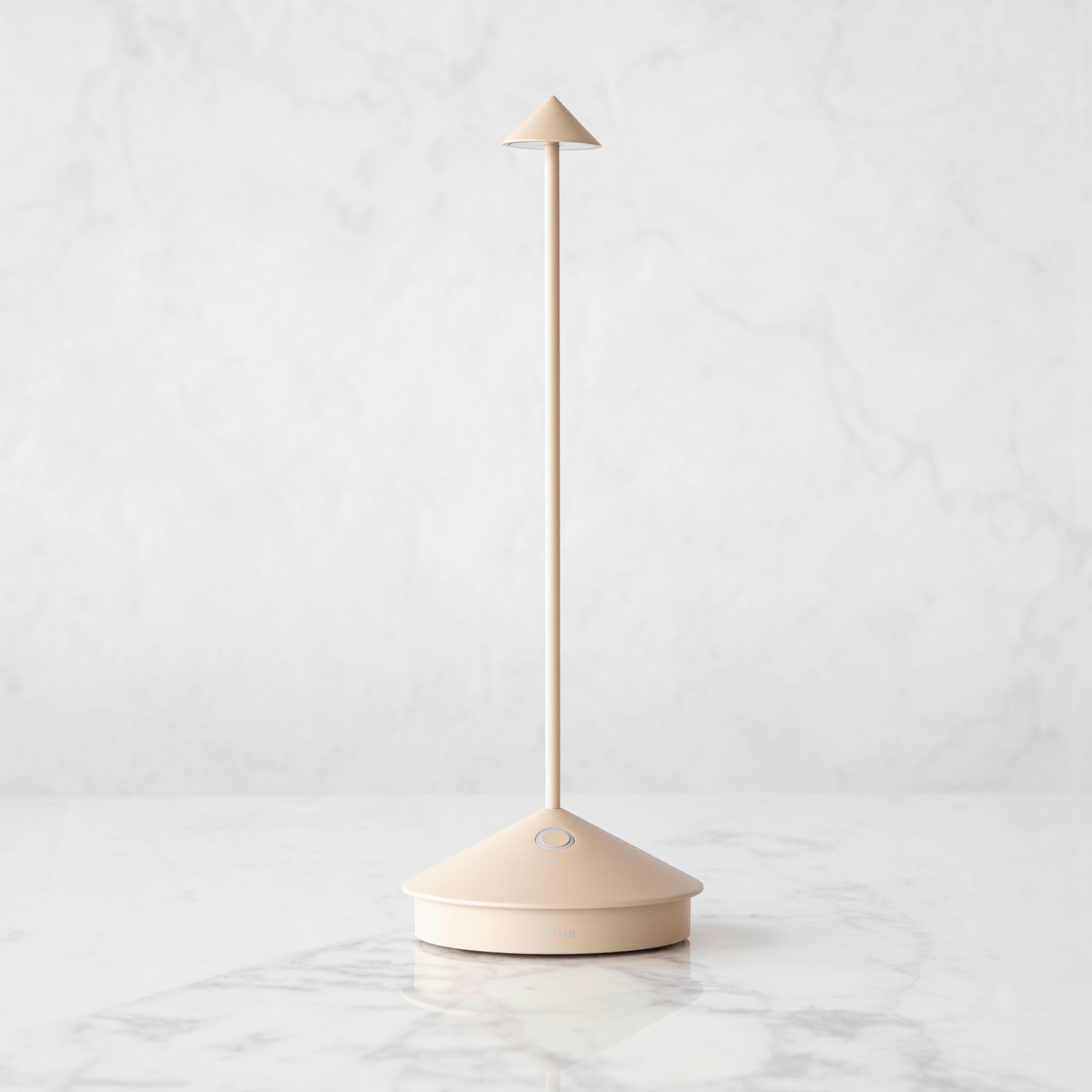 A Sand LED Cordless Lamp by Zafferano on a table next to a book and a plant.