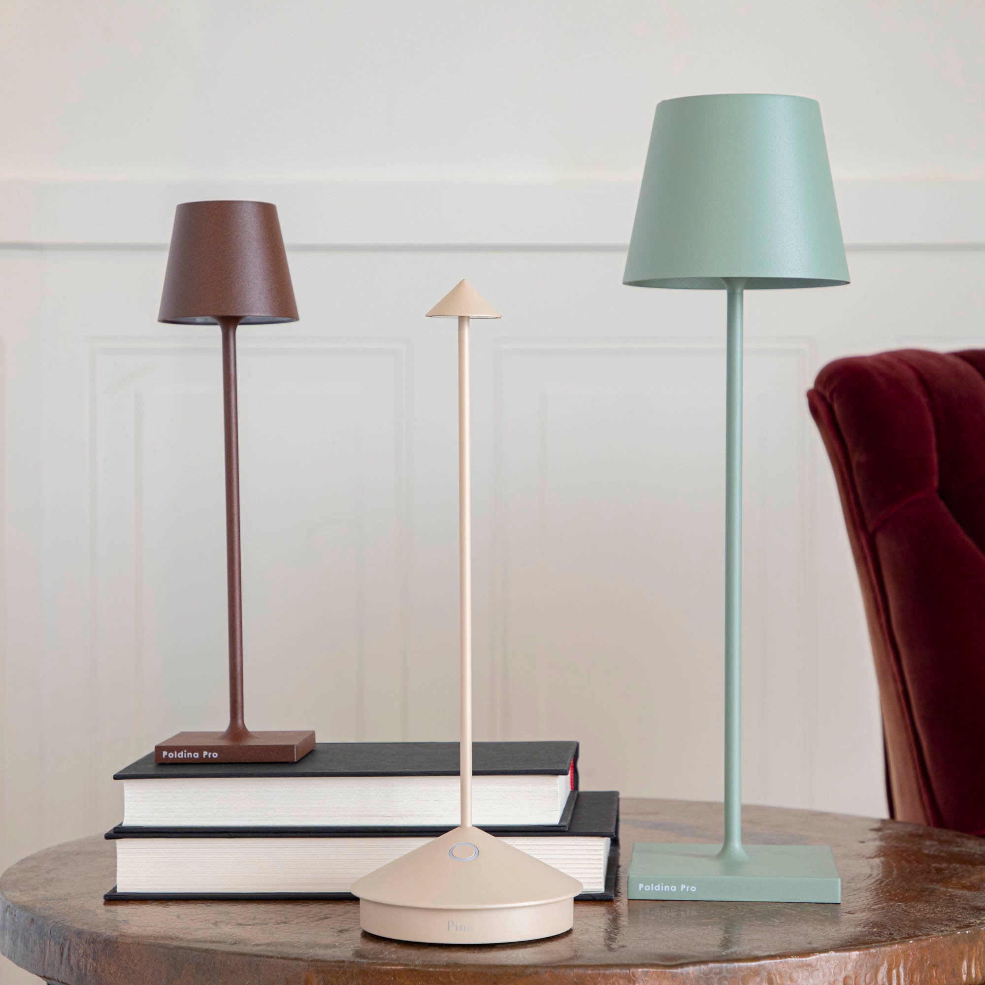 A Sage Micro Cordless Lamp by Zafferano on a table next to a book and a plant.