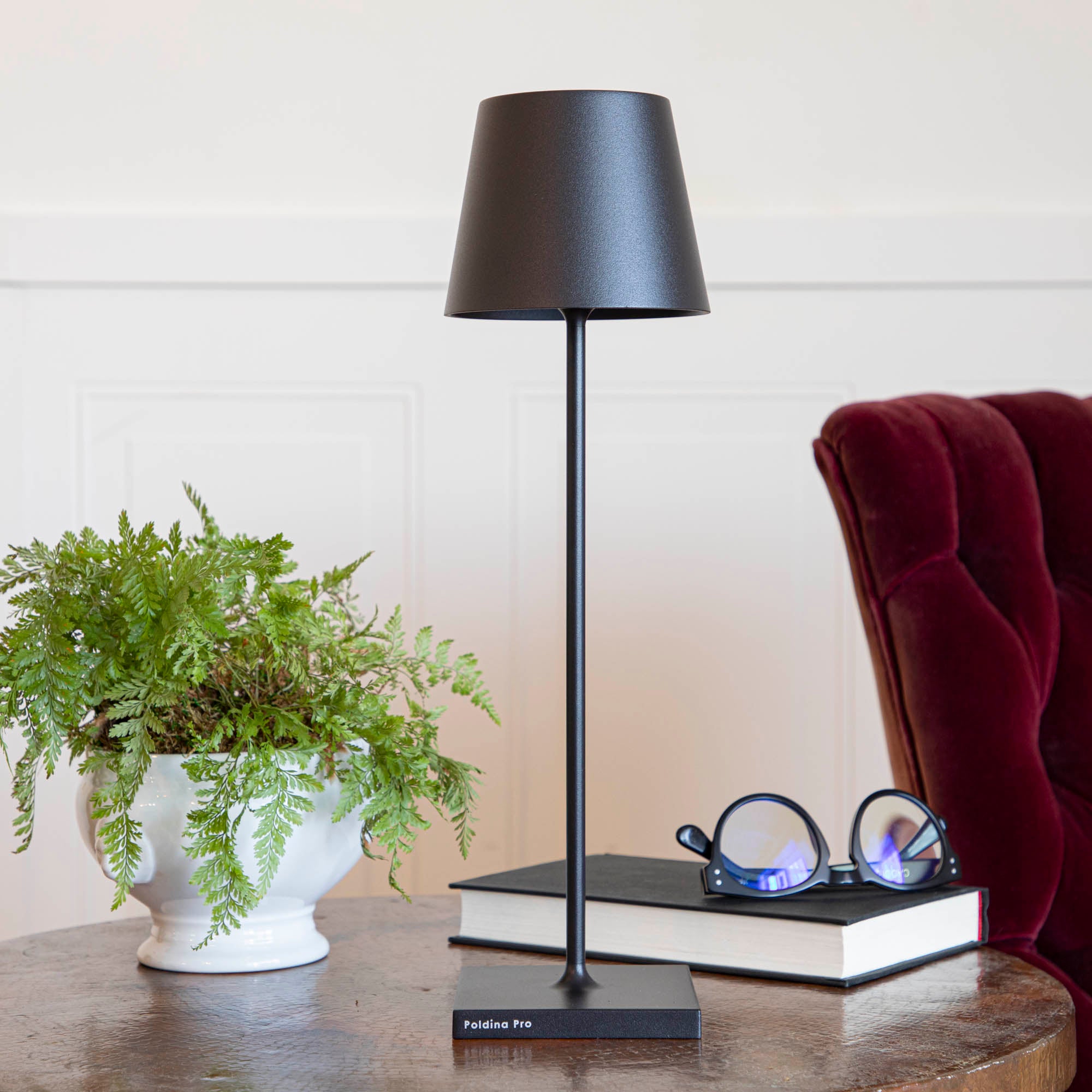 A Black Cordless Lamp by Zafferano on a table next to a book and a plant.