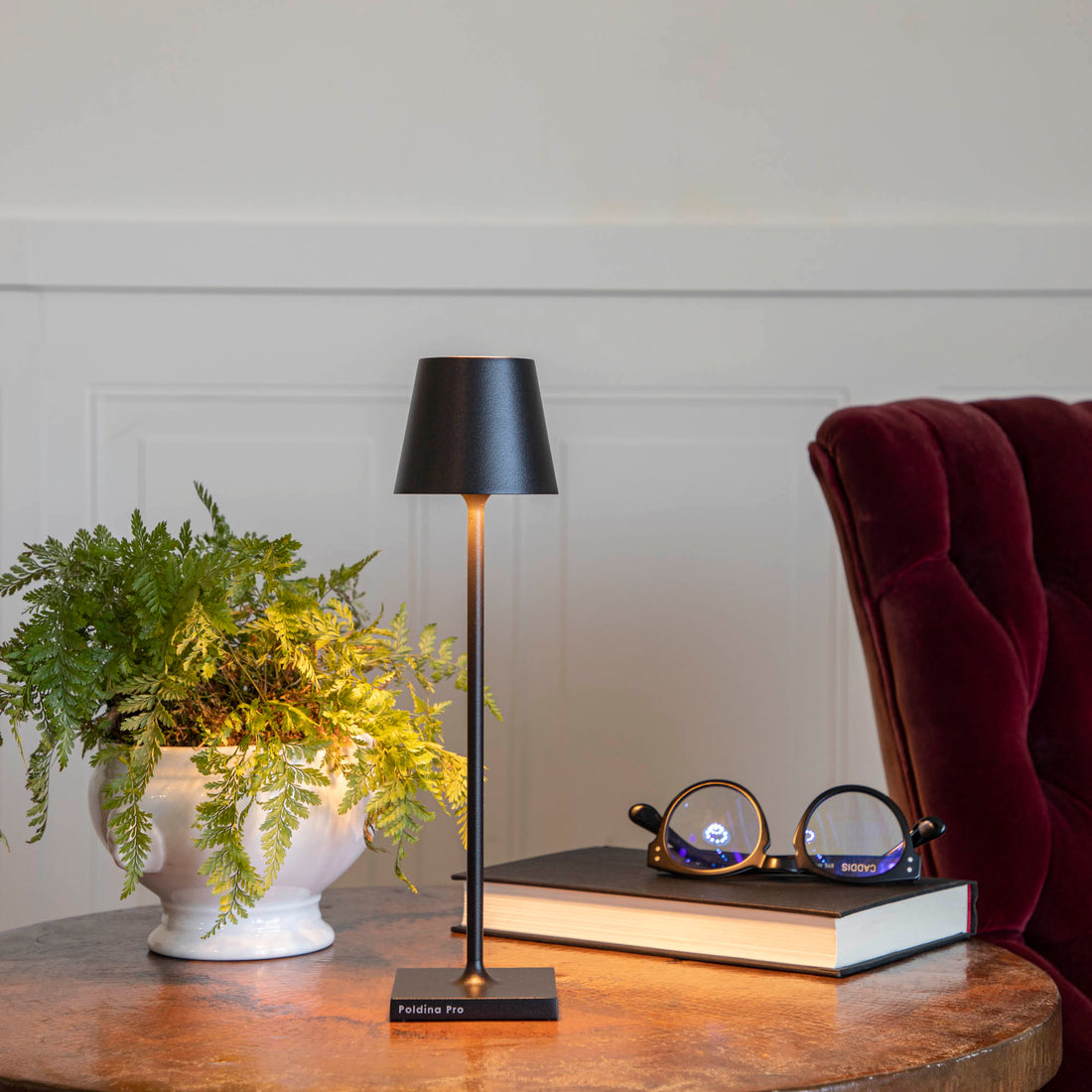 A Zafferano Black Micro Cordless Lamp on a table next to a book and a plant.