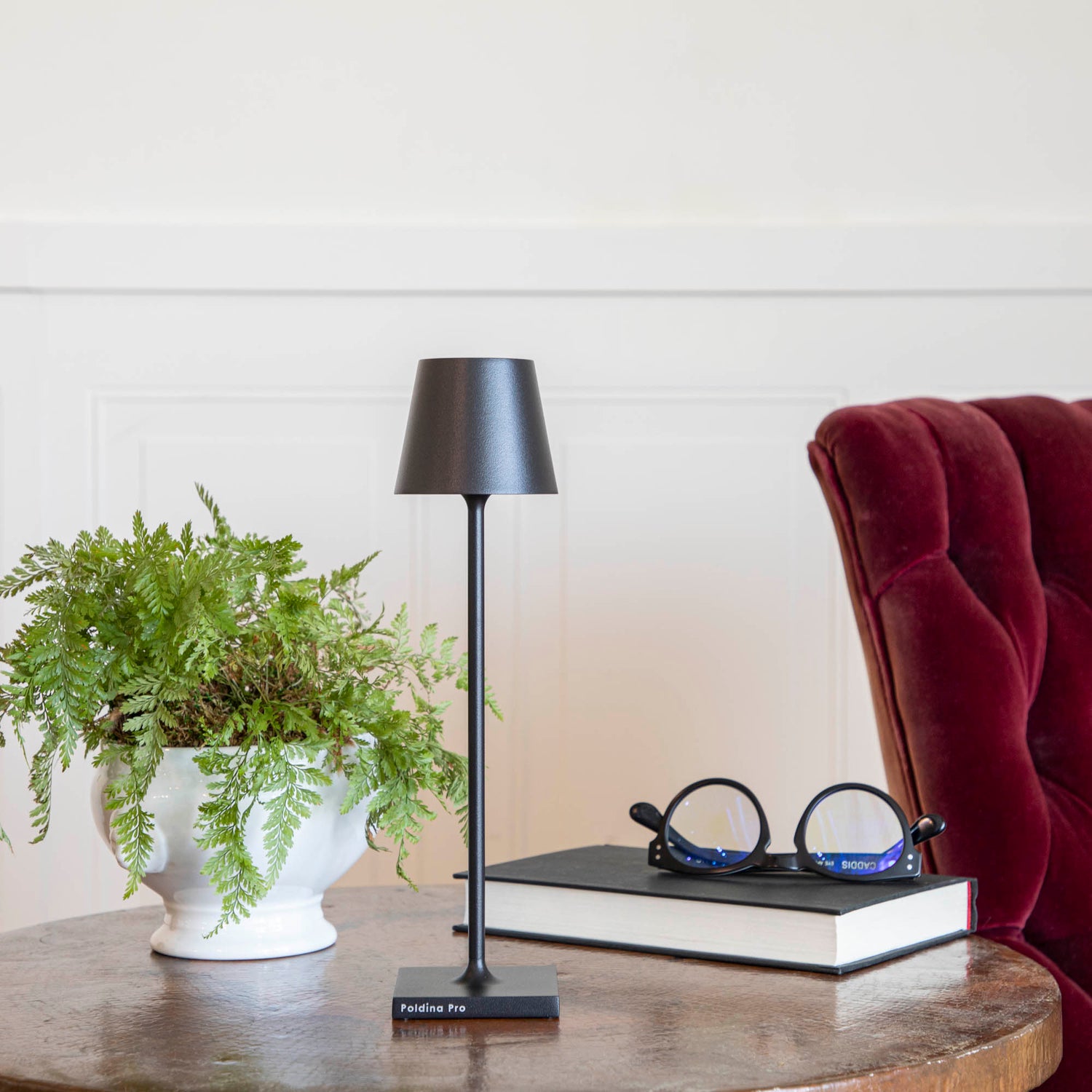 A Zafferano Black Micro Cordless Lamp on a table next to a book and a plant.