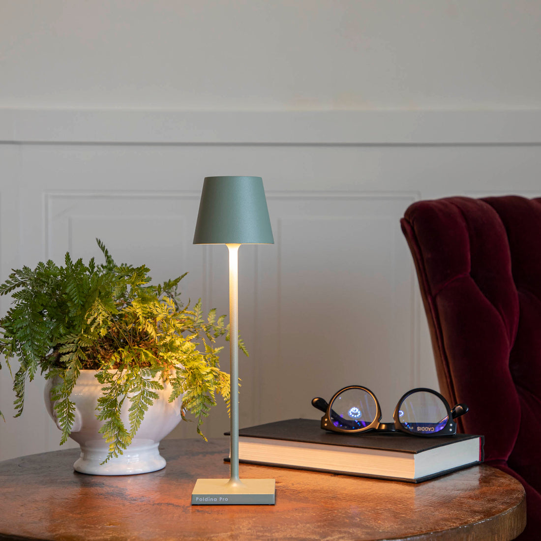 A Sage Micro Cordless Lamp by Zafferano on a table next to a book and a plant.