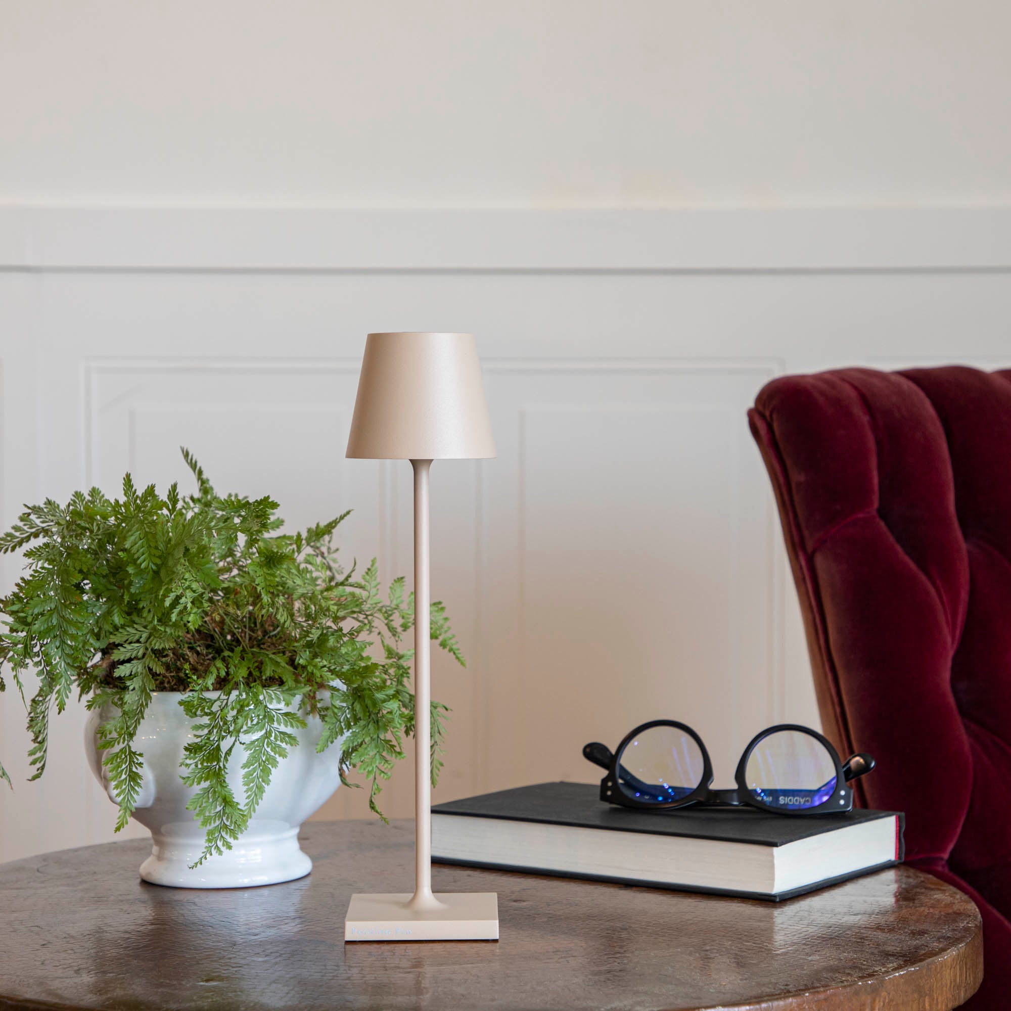 A Sand Micro Cordless Lamp by Zafferano on a table next to a book and a plant.