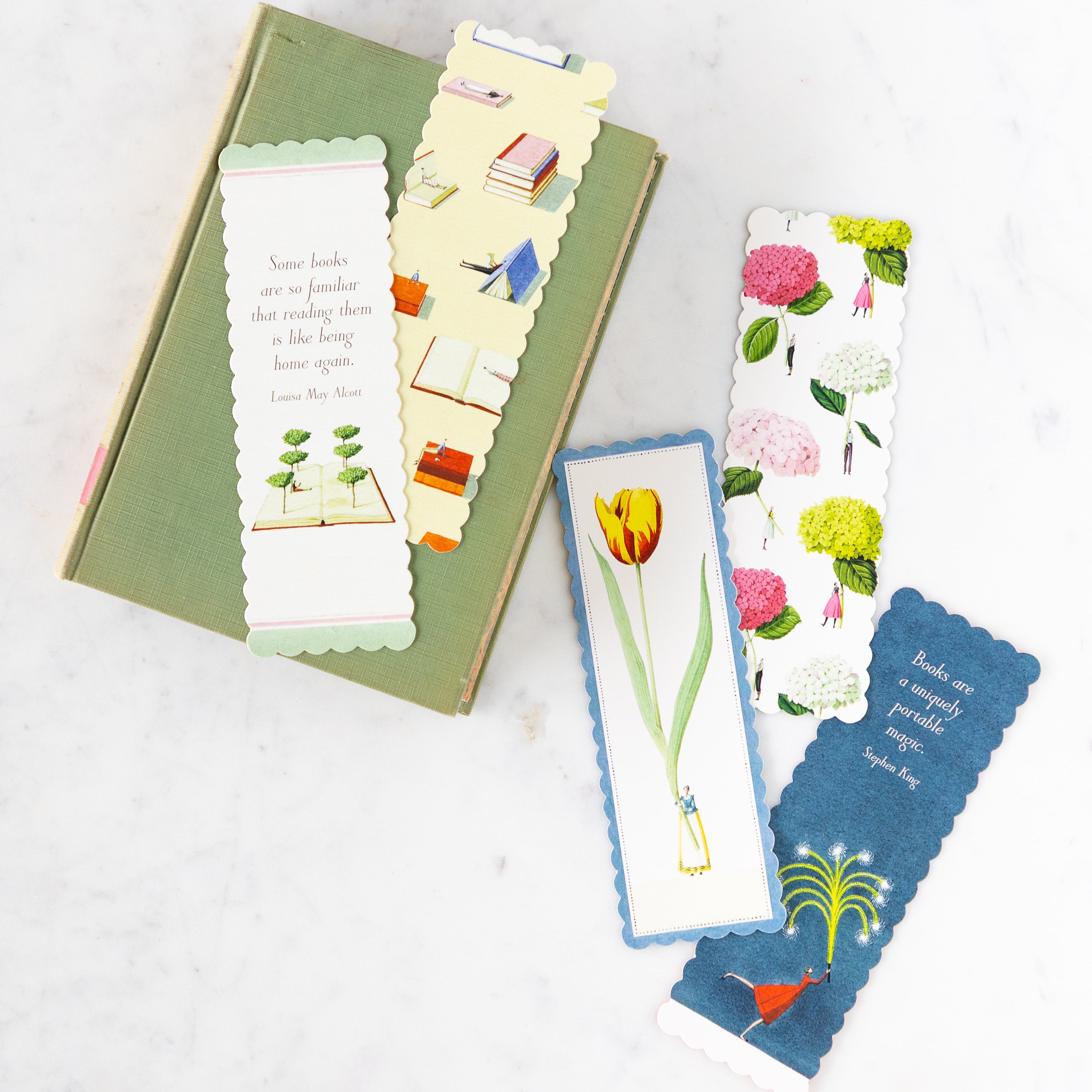 A green book on a marble table with Laura Stoddart designed bookmarks scattered across the book and table.