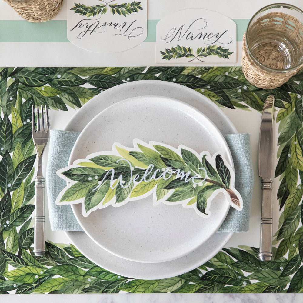 An elegant place setting featuring a Laurel Table Accent with "Welcome" written on it in white ink resting on the plate, from above.