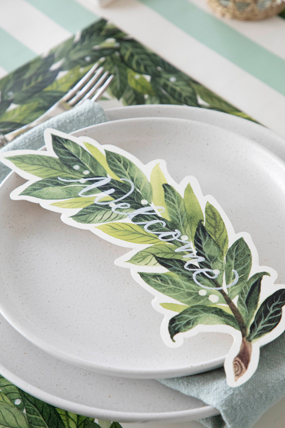 An elegant place setting featuring a Laurel Table Accent with &quot;Welcome&quot; written on it in white ink resting on the plate.