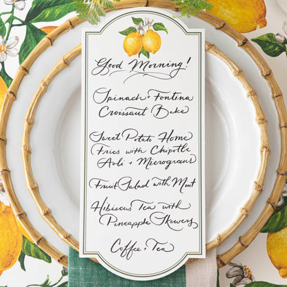 Top-down view of a bright citrus-themed place setting featuring a Lemon Table Card with a menu written on it resting on the plate.