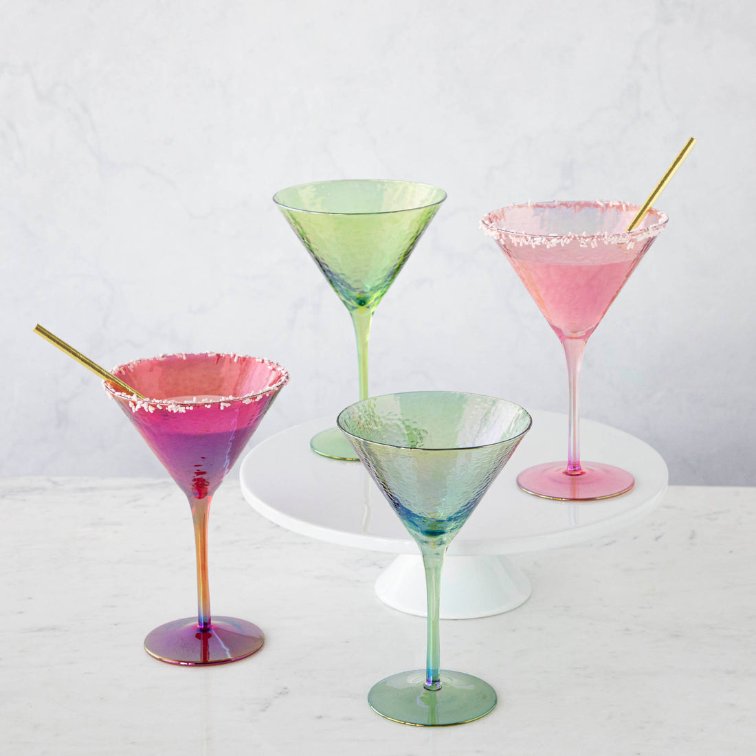 Four stylish Luster Aperitivo Martini Glasses in Zodax with sugar rims on a white stand against a marble background.