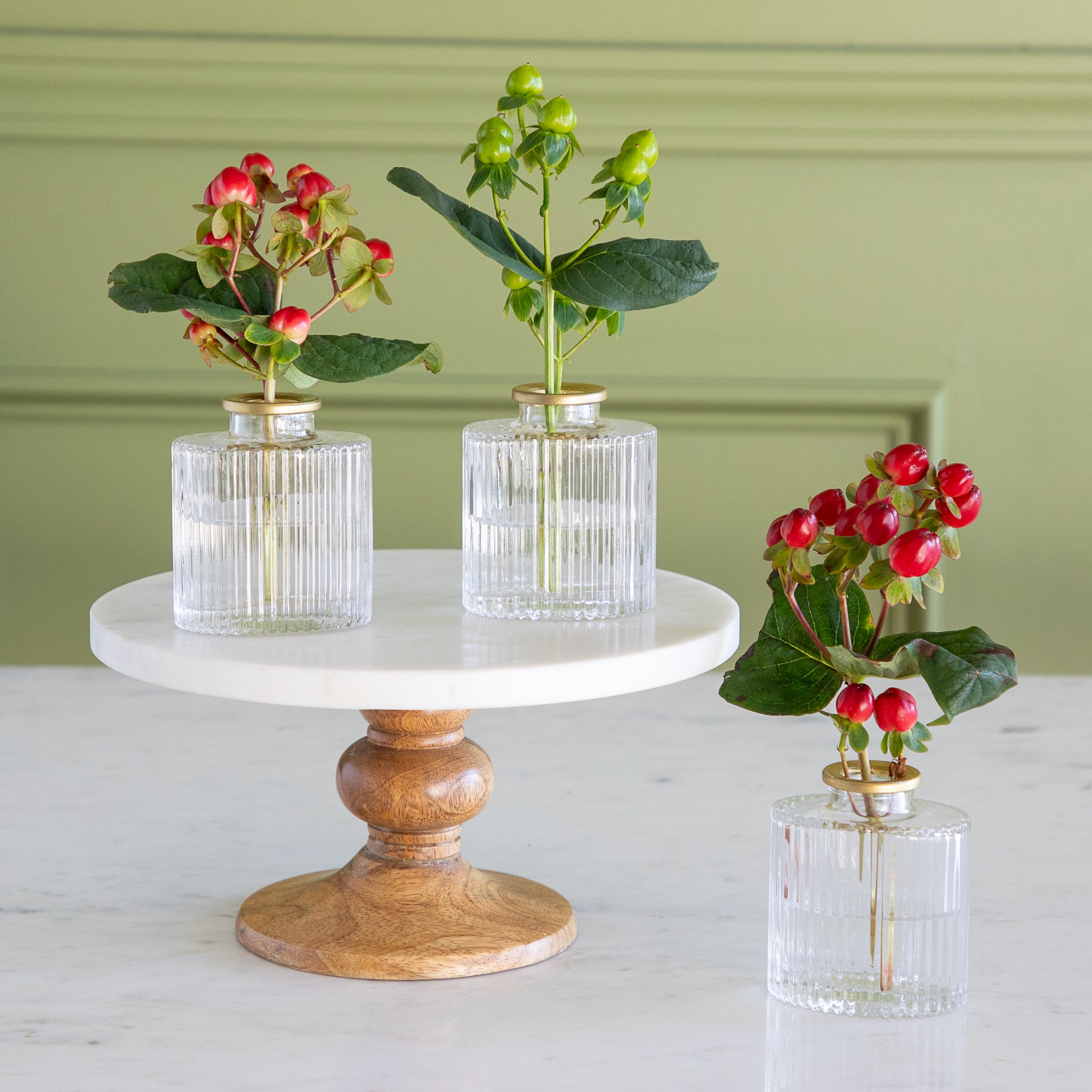 Three small glass vases with plants on a marble stand against a green wall.