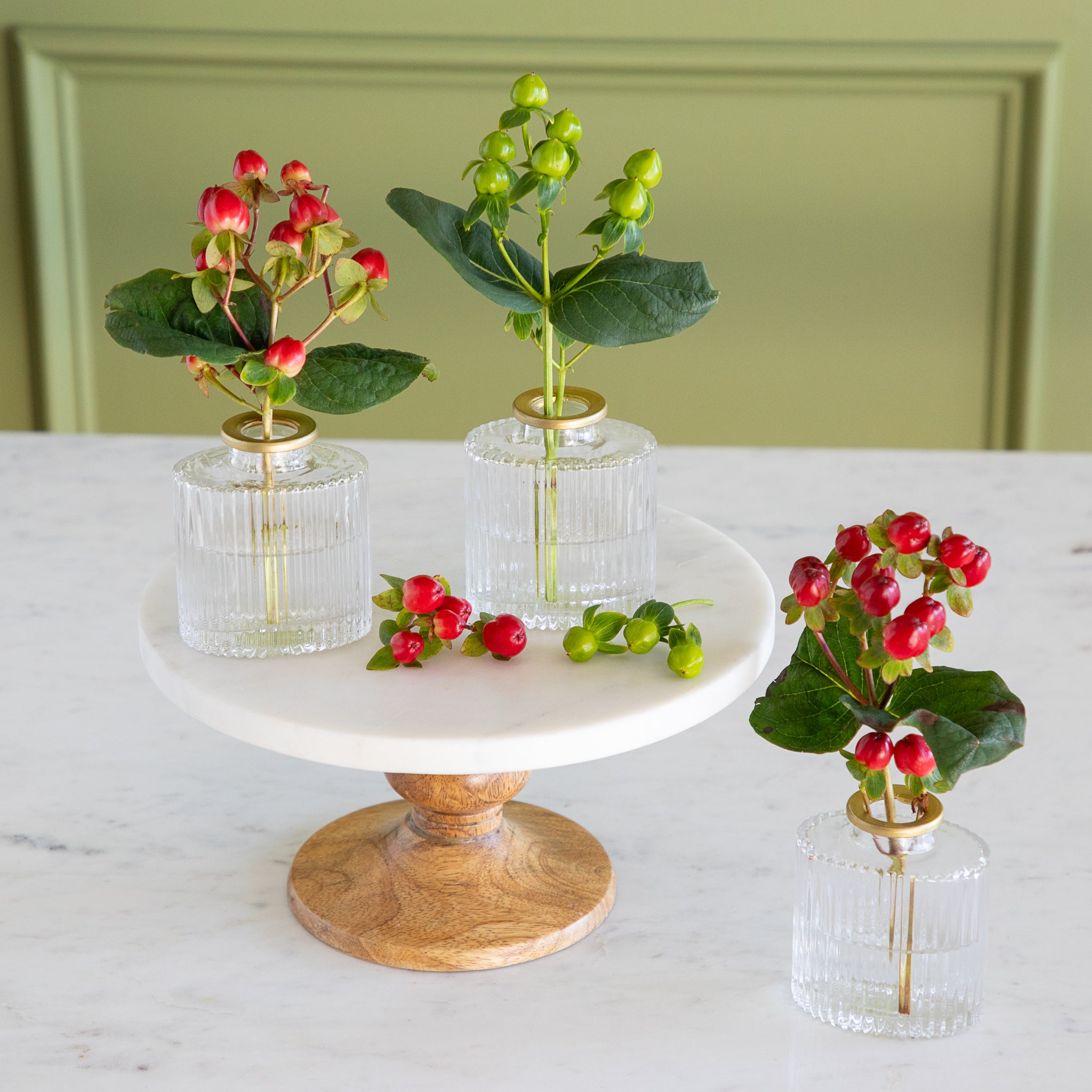 Decorative setup with small plants in clear vases on a marble stand against a light green wall.