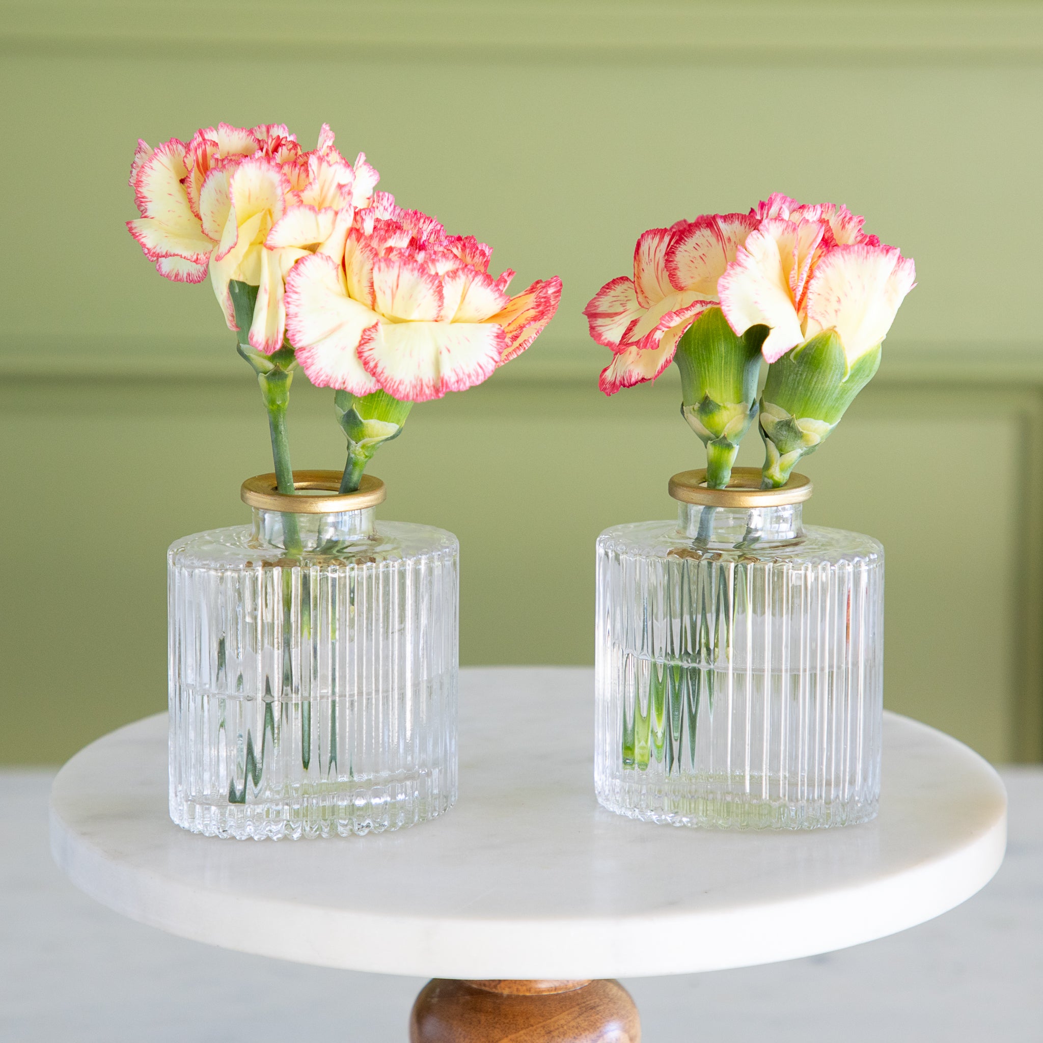 Two clear glass vases with holding pink and white flowers on a white surface with a green background.