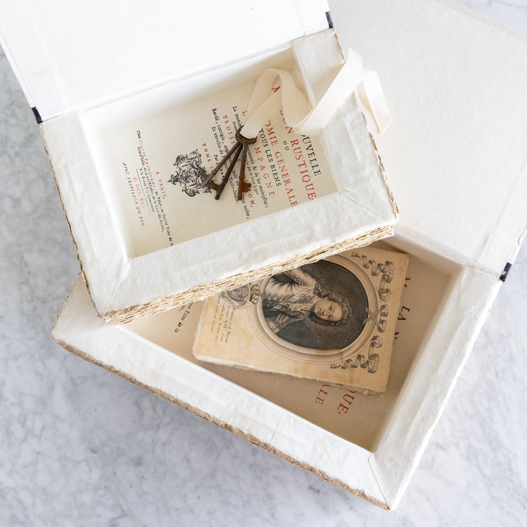 Two open storage boxes with a vintage book inside one and vintage keys in the other.