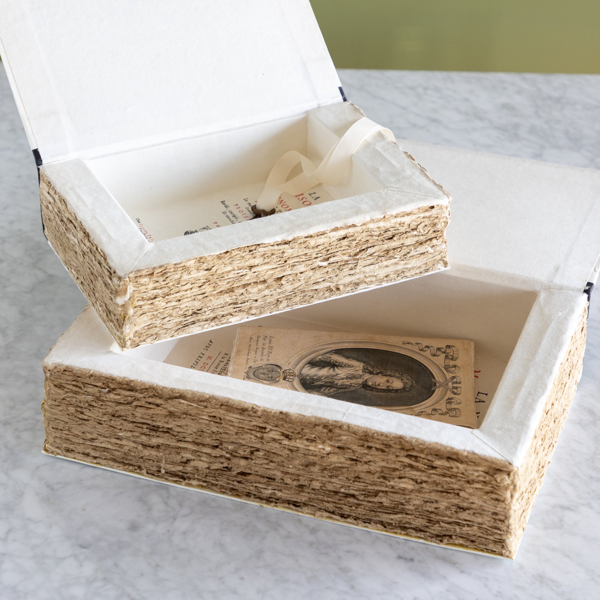 Two stacked decorative boxes with textured paper design on a marble surface.