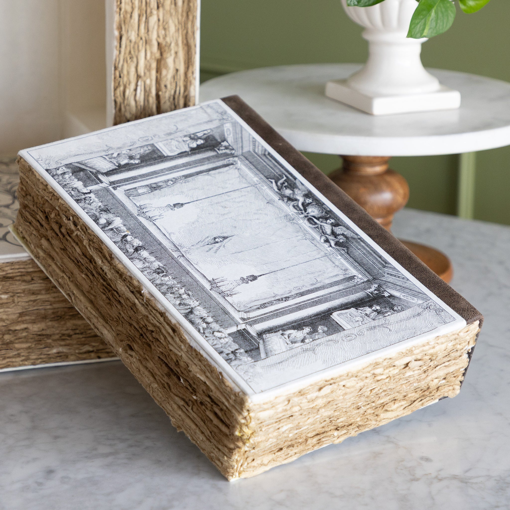 Theater Book of Secrets, a decorative storage box resembling a book featuring a vintage illustration of a theater scene, on a marble table.