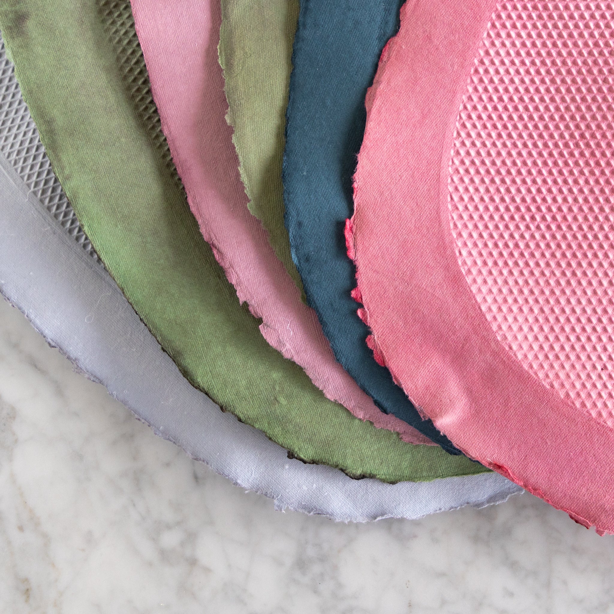 Stack of Multicolored Paper Placemats fanned out on a marble table.