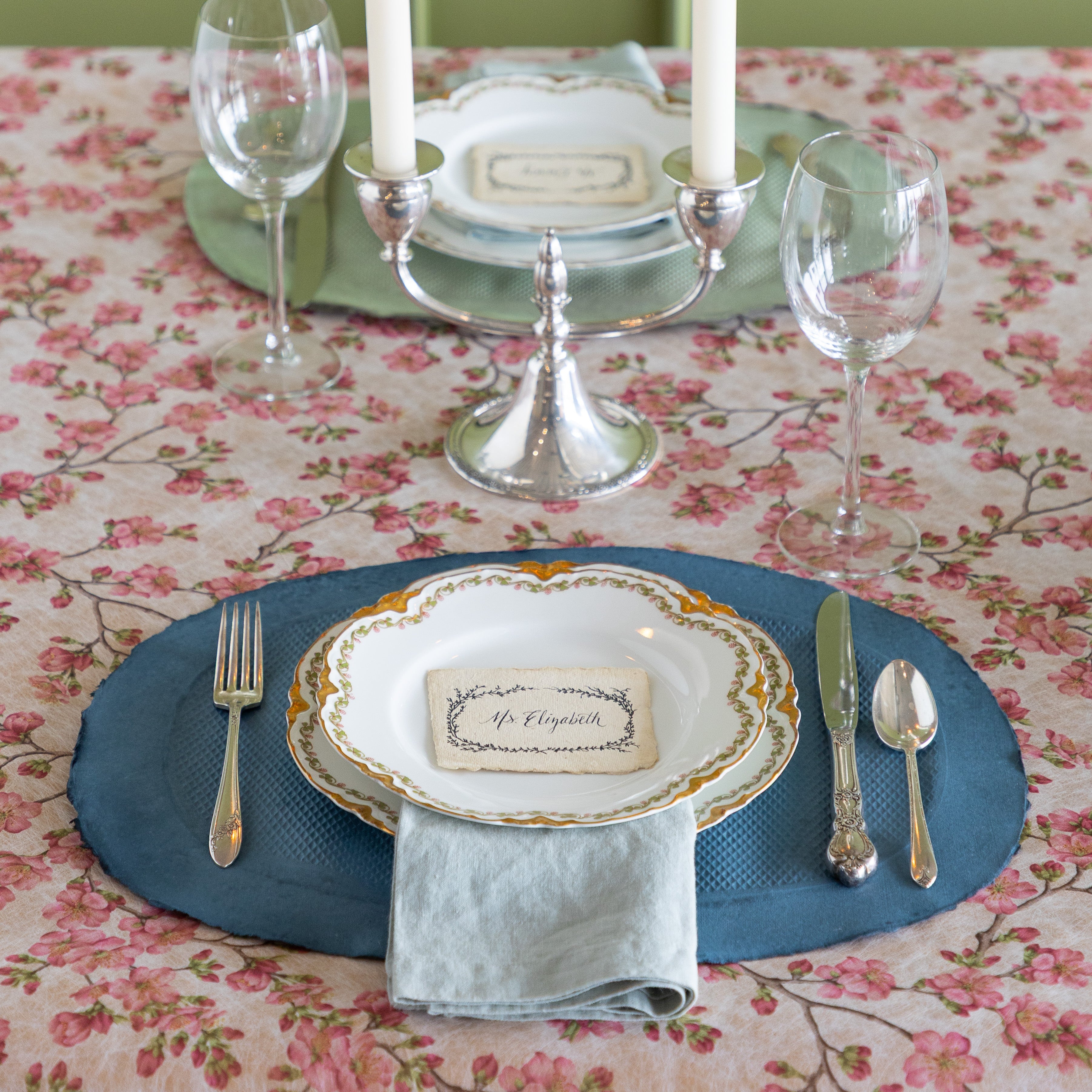 Elegant table setting with blue and green paper placemats, candles, and silverware on the Pink Cherry Blossom Runner.