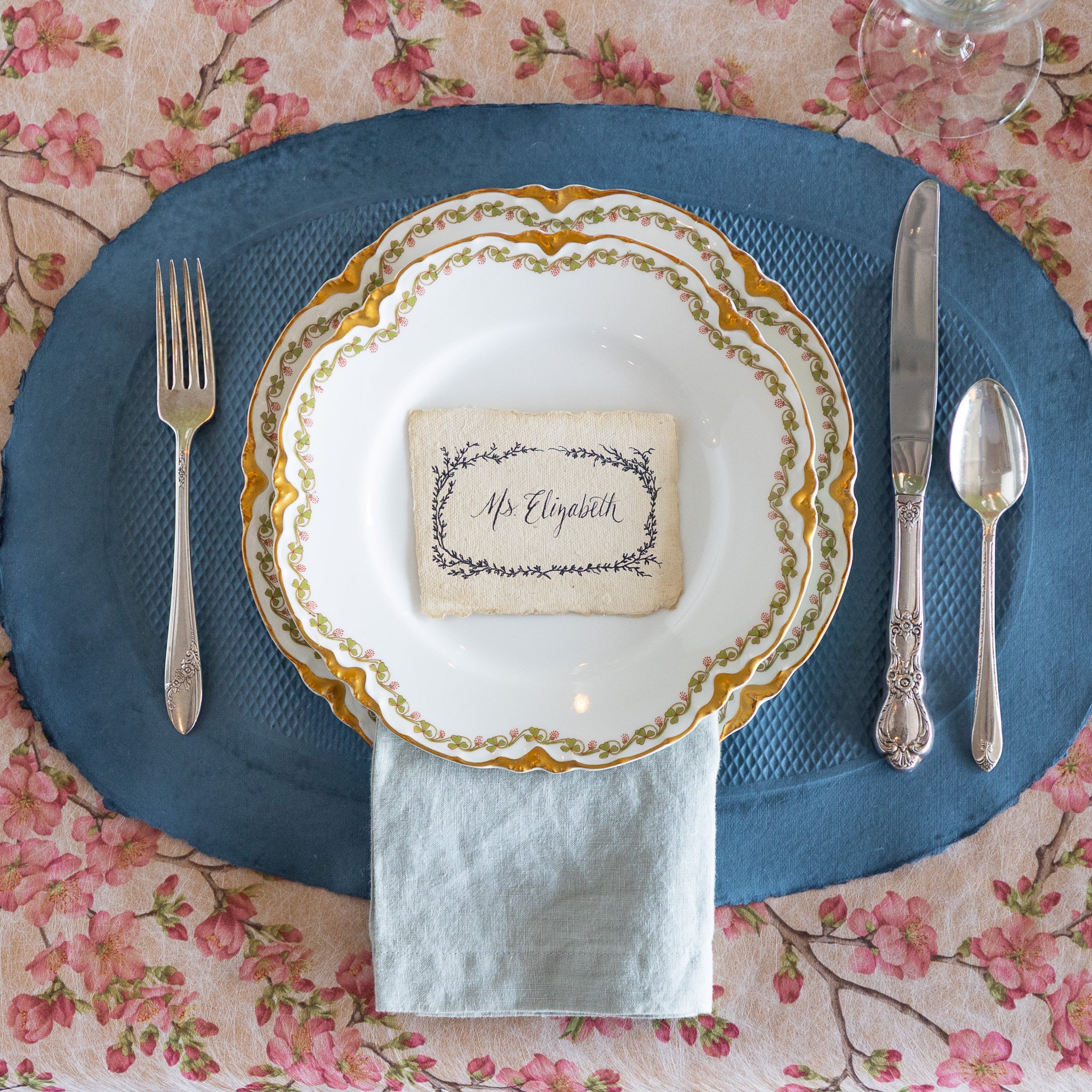 Elegant table setting with a blue paper placemat, vintage dinnerware and silverware on the Pink Cherry Blossom Runner.