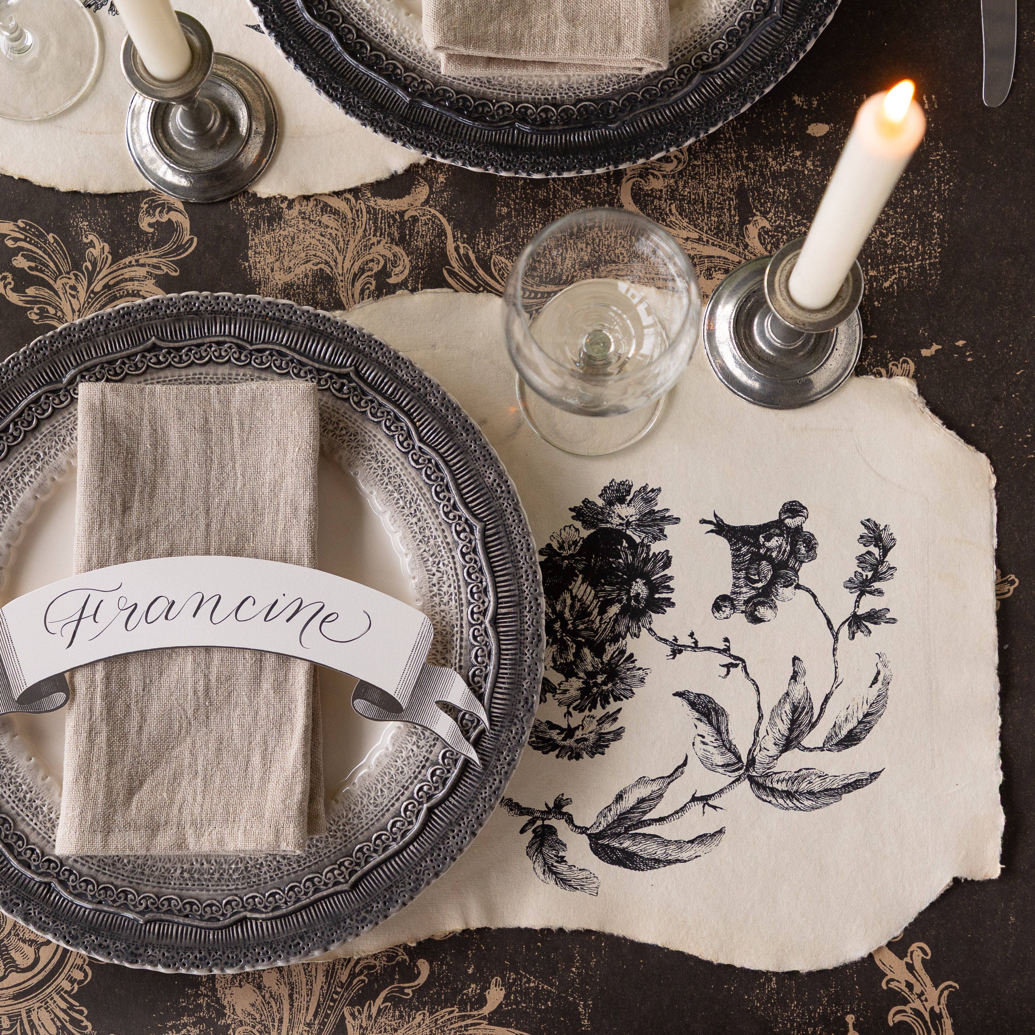 Elegant place setting with decorative plates, Pillement Paper Placemats, Classic Banner Table Accent, glasses, and candles on the Black Archival Runner.