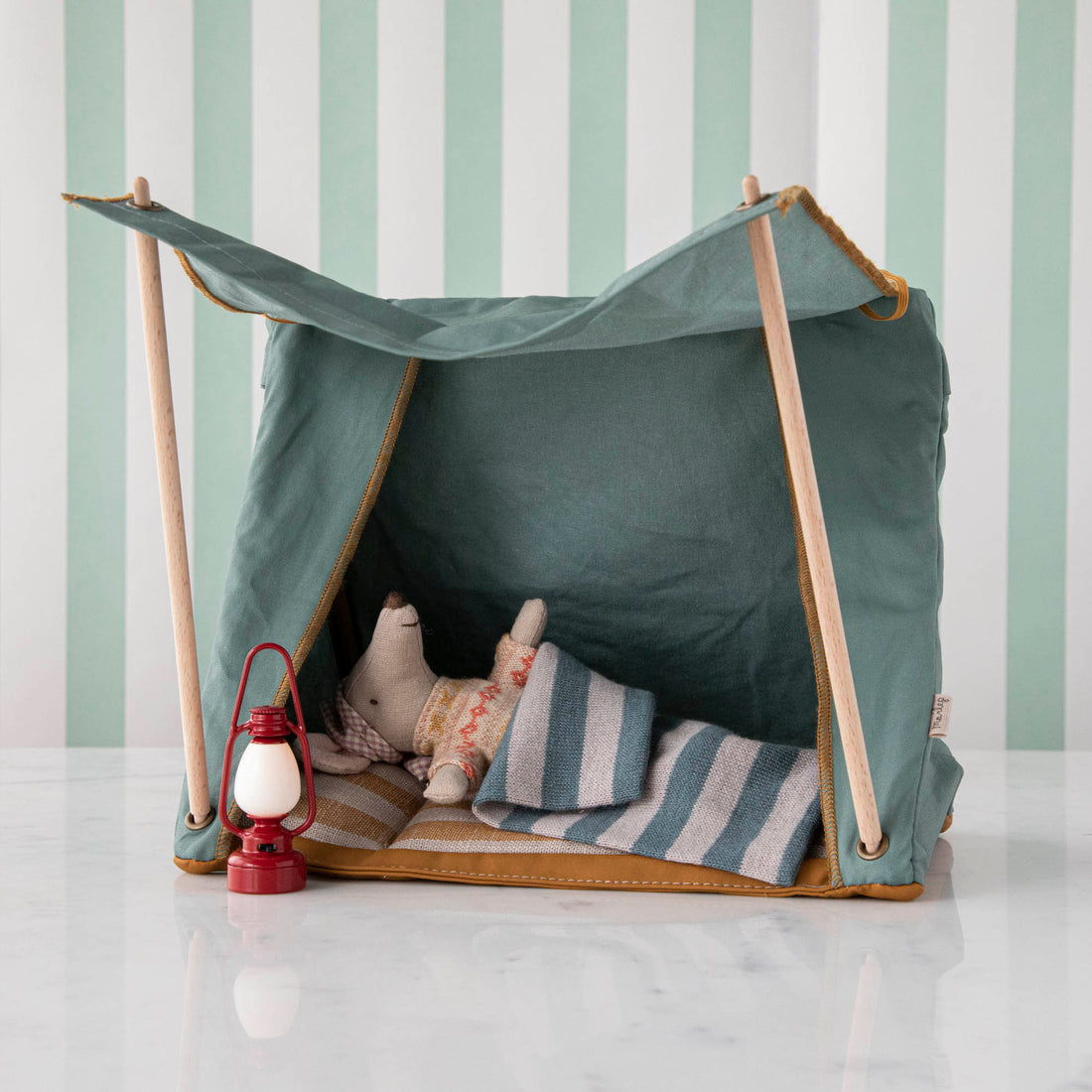 A homemade tent for children made from blankets and wooden sticks, with a Maileg Vintage Lantern and cushions inside.
