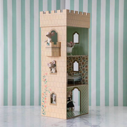 A whimsical multi-level Maileg Mouse Castle with kitchen, adorned with decorative elements, placed against a striped wall.