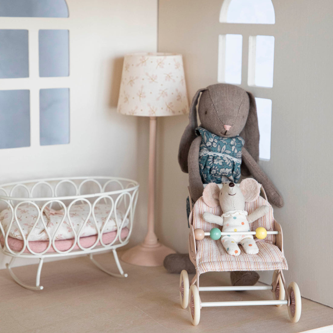Plush rabbit toys staged in a dollhouse setting with a miniature crib, lamp, and Maileg Baby Mice Stroller.
