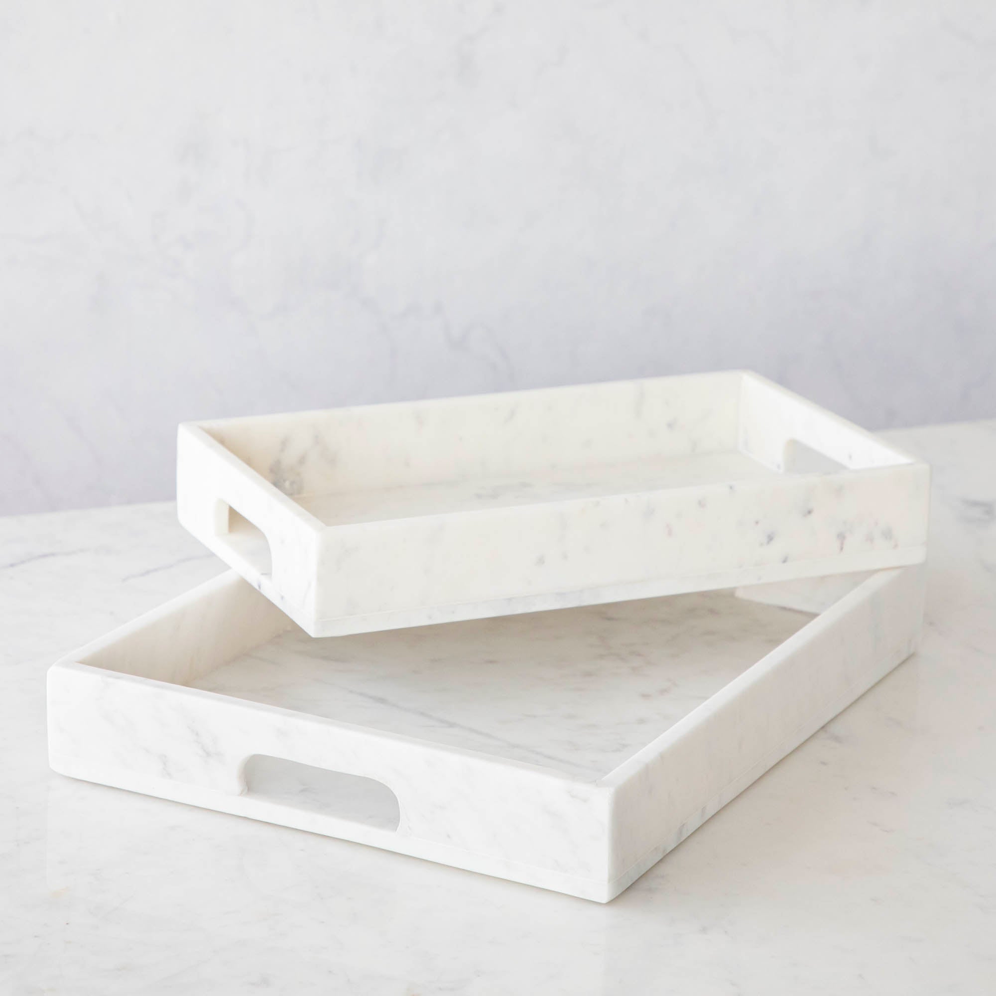 Two Godinger White Marble Rectangular Trays on a striped surface, one holding art supplies and the other candles and a small jar, showcasing the elegance of marble.