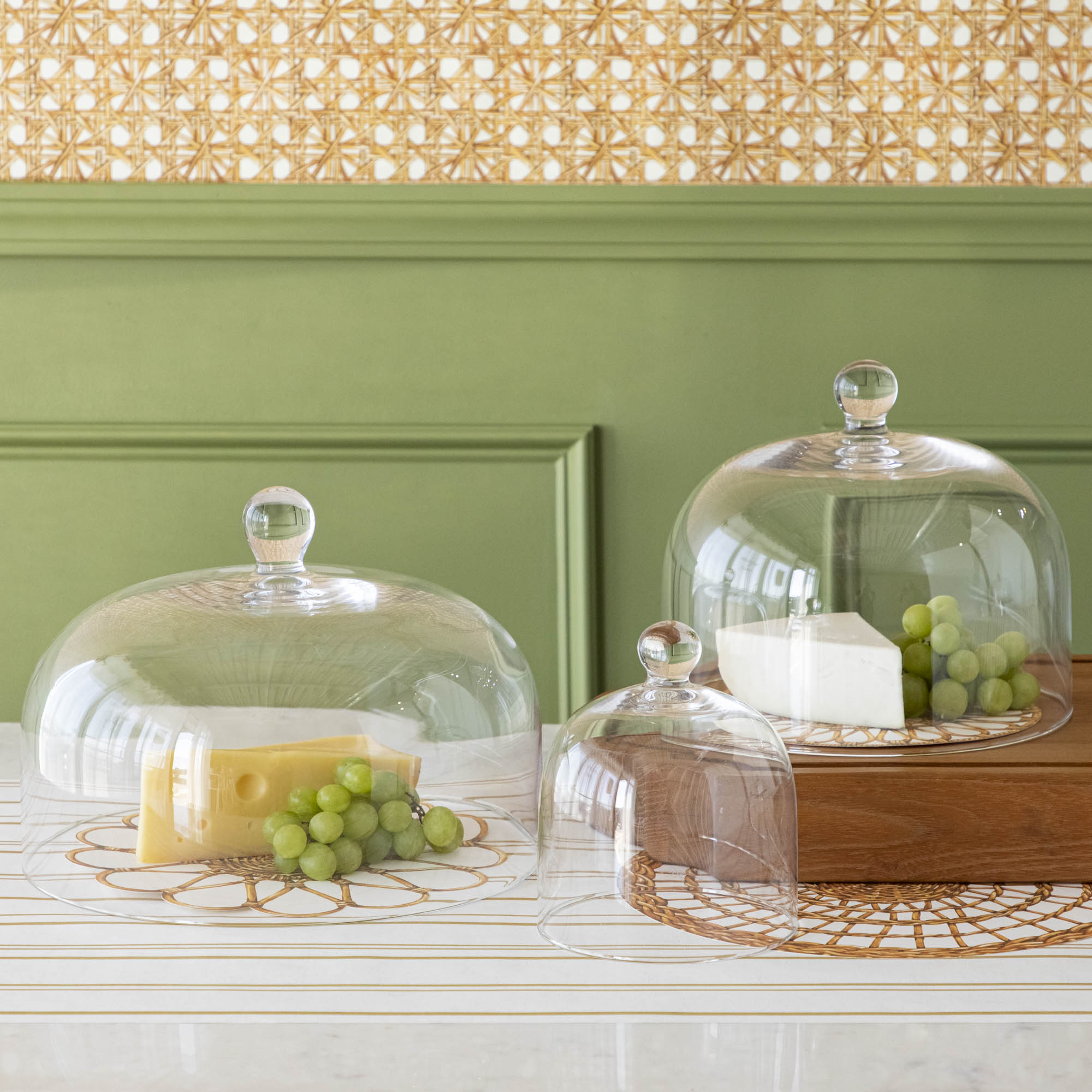 Various cheeses and grapes displayed under a Casafina Living glass dome serveware on a kitchen counter.