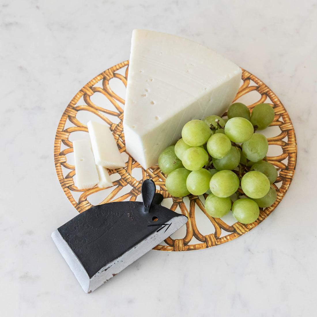 A plate with a wedge of cheese, a bundle of green grapes, and a Magenta Wrought Iron Mouse Cheese Blade.