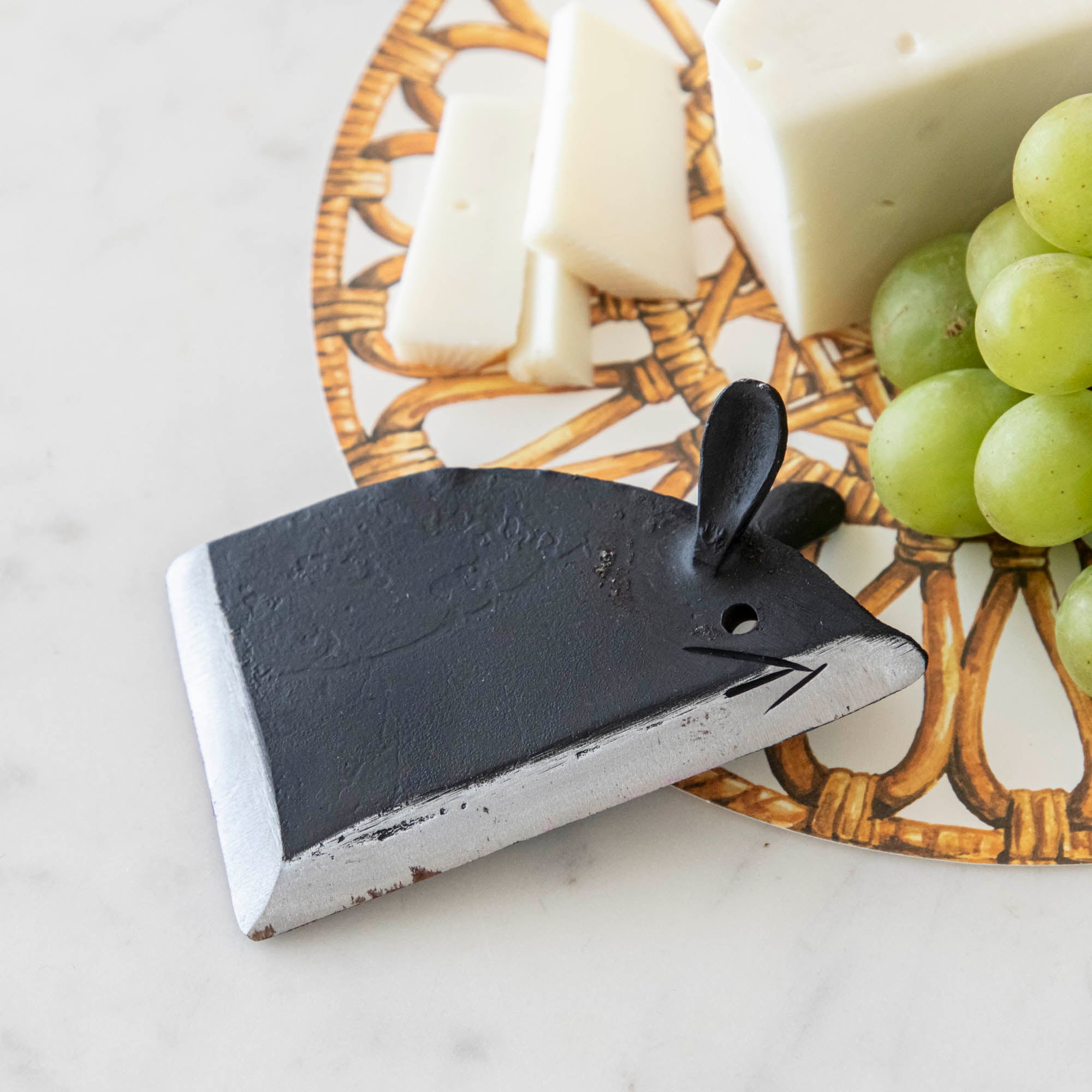 Cheese and grapes on a plate with a cheese knife shaped like a mouse on a marble surface.