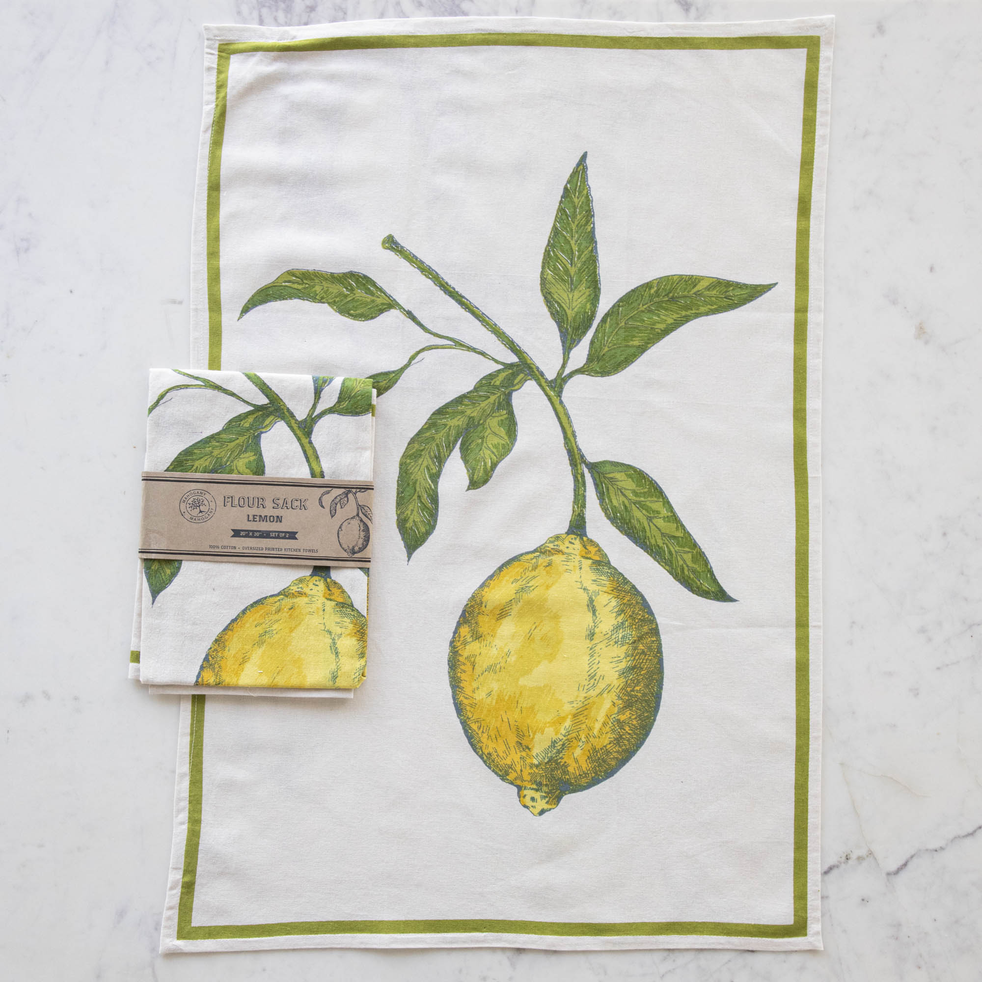 A Lemon Flour Sack Kitchen Towel Set of 2 with a lemon design hanging on a wooden deck railing, with a bowl of lemons in the background. (Mahogany)