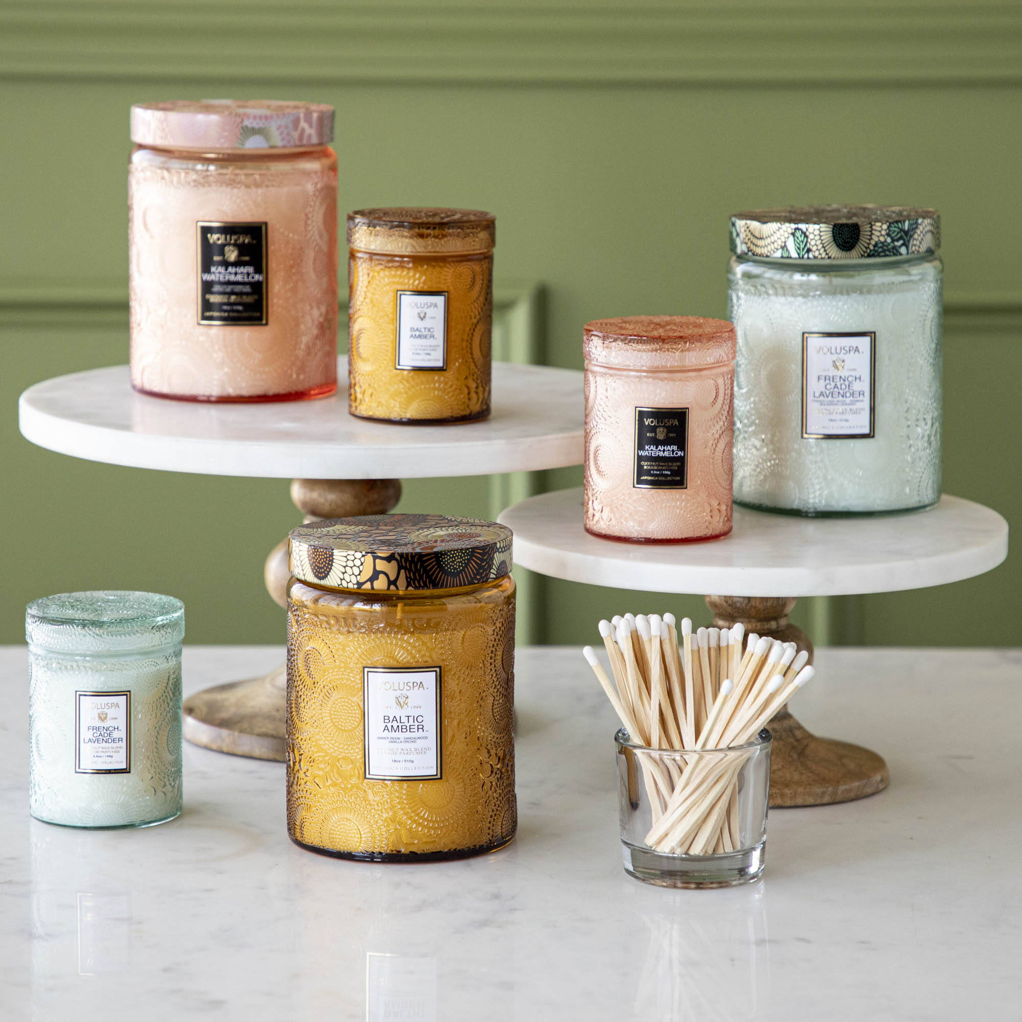 Two Voluspa Kalahari Watermelon candles on a marble surface with matches nearby, featuring a crisp cucumber aroma.