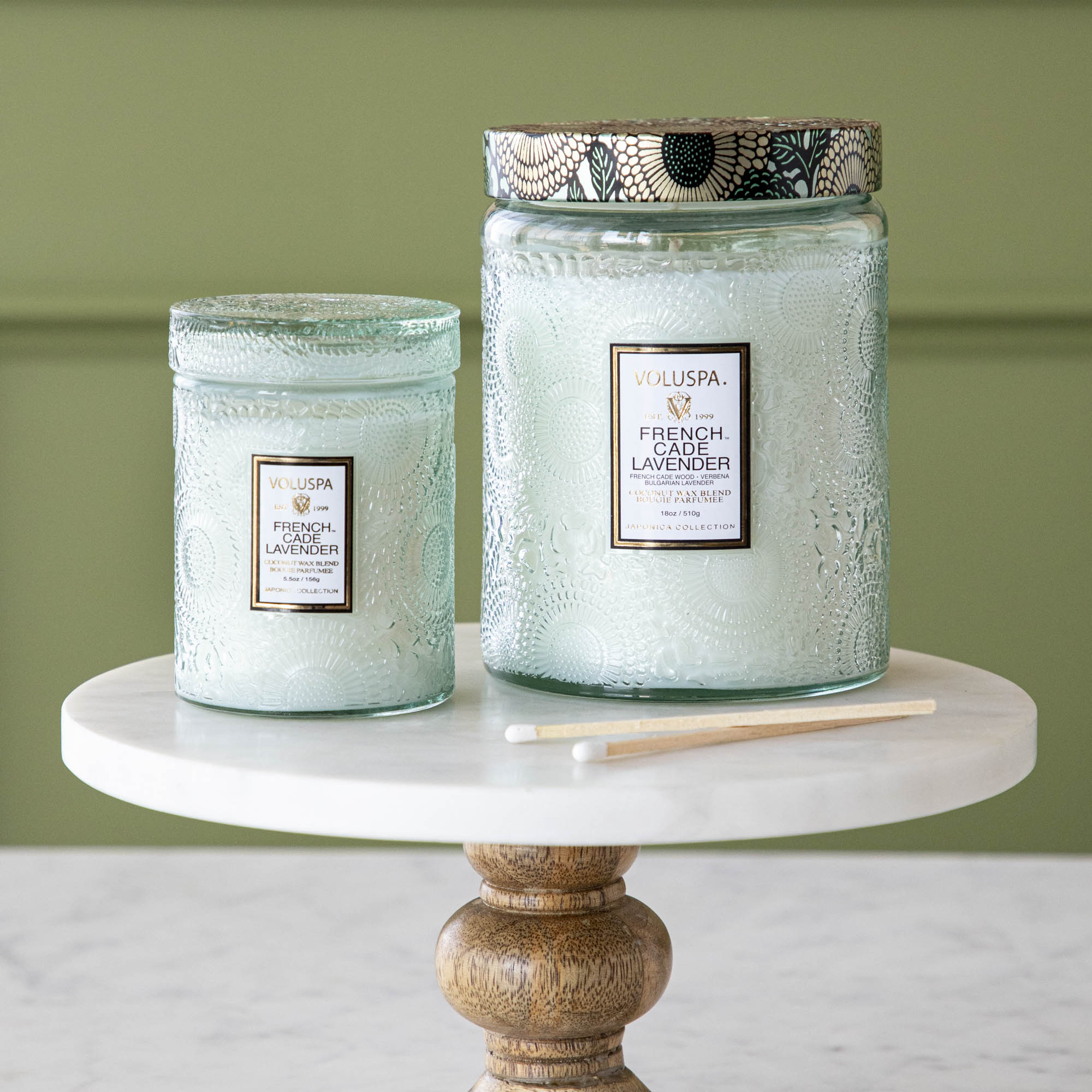 Two Voluspa French Cade Lavender candles on a marble surface with lemon verbena matchsticks.